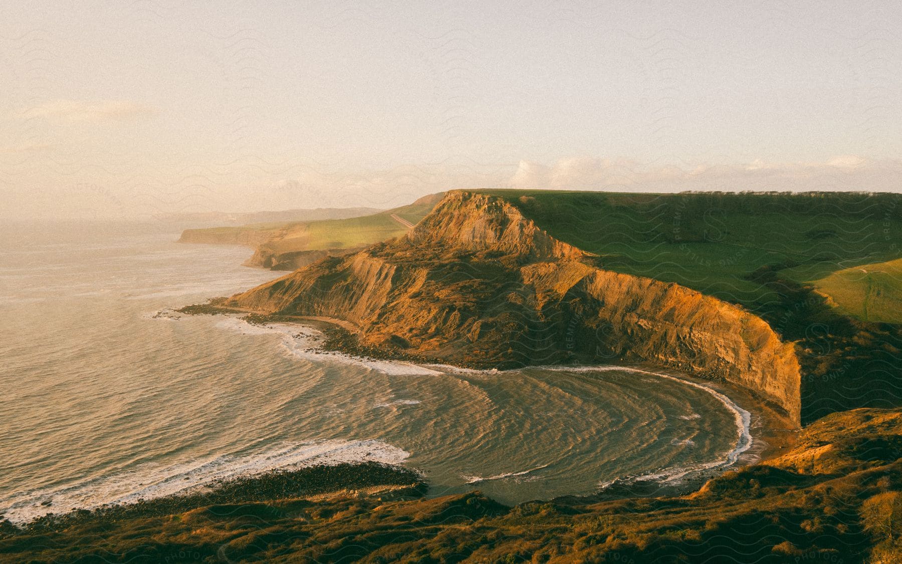 An island with a rocky shoreline, where waves from the ocean crash against the rocks on a sunny day.