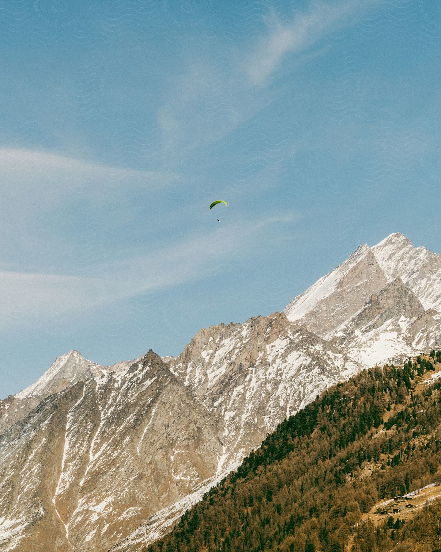Natural scenery of mountains with snow and vegetation and a person with a parachute in the blue sky
