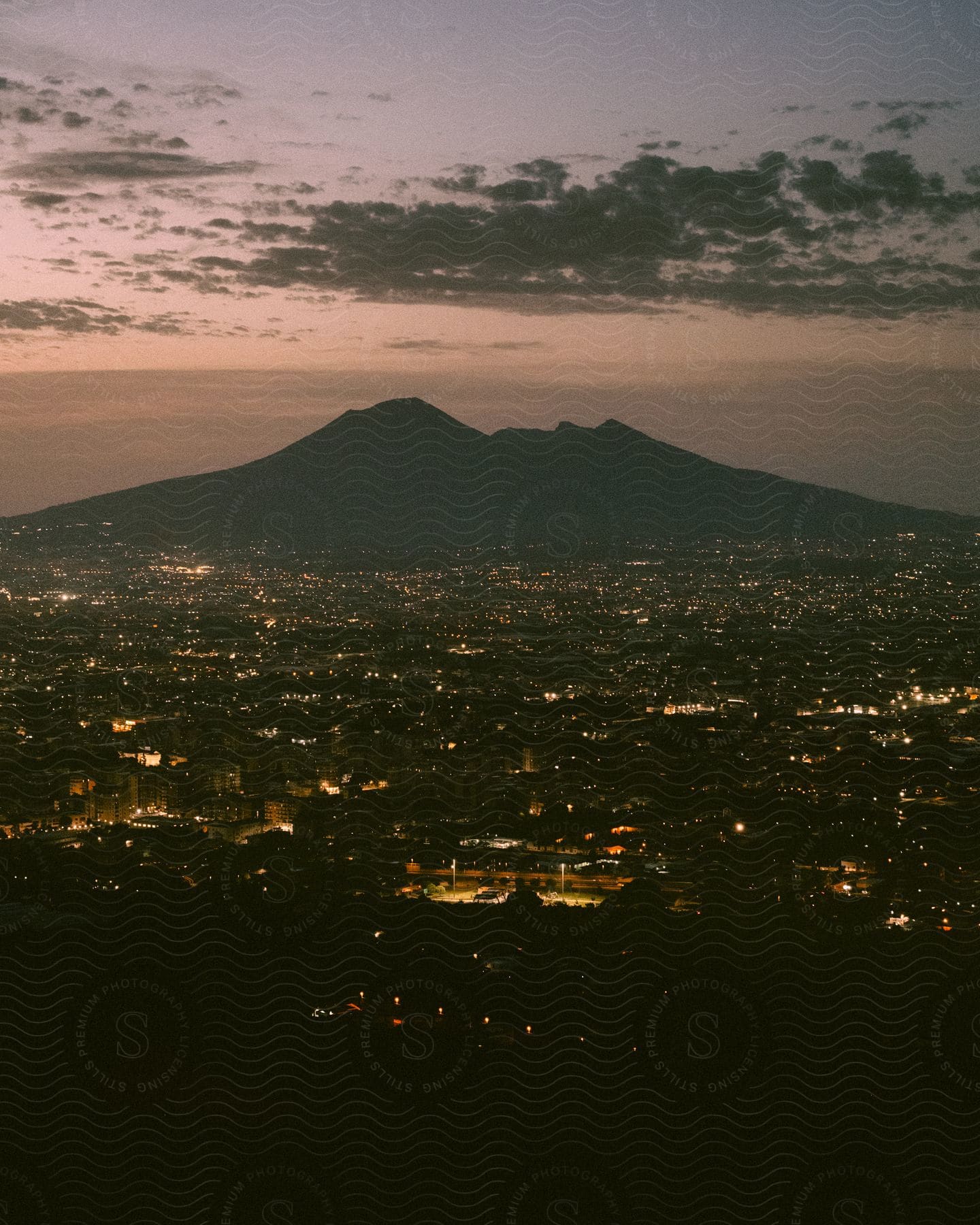 Lights glow in the city along the coast as clouds float over the mountains in the distance