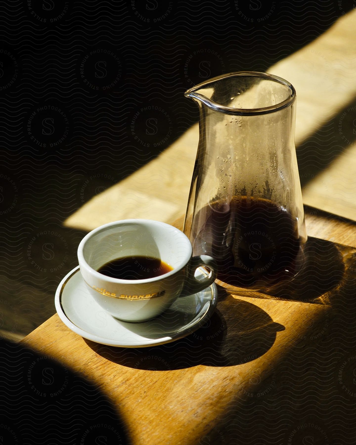 A white coffee cup with saucer and a glass carafe on a wooden surface.