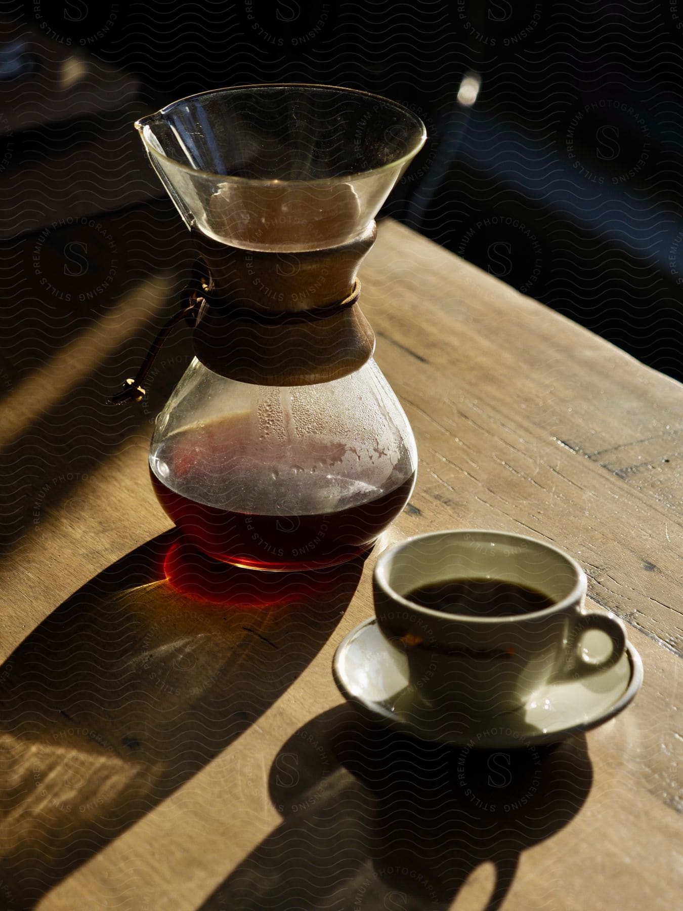 Pour over coffee maker stands on wooden table with a cup of coffee.