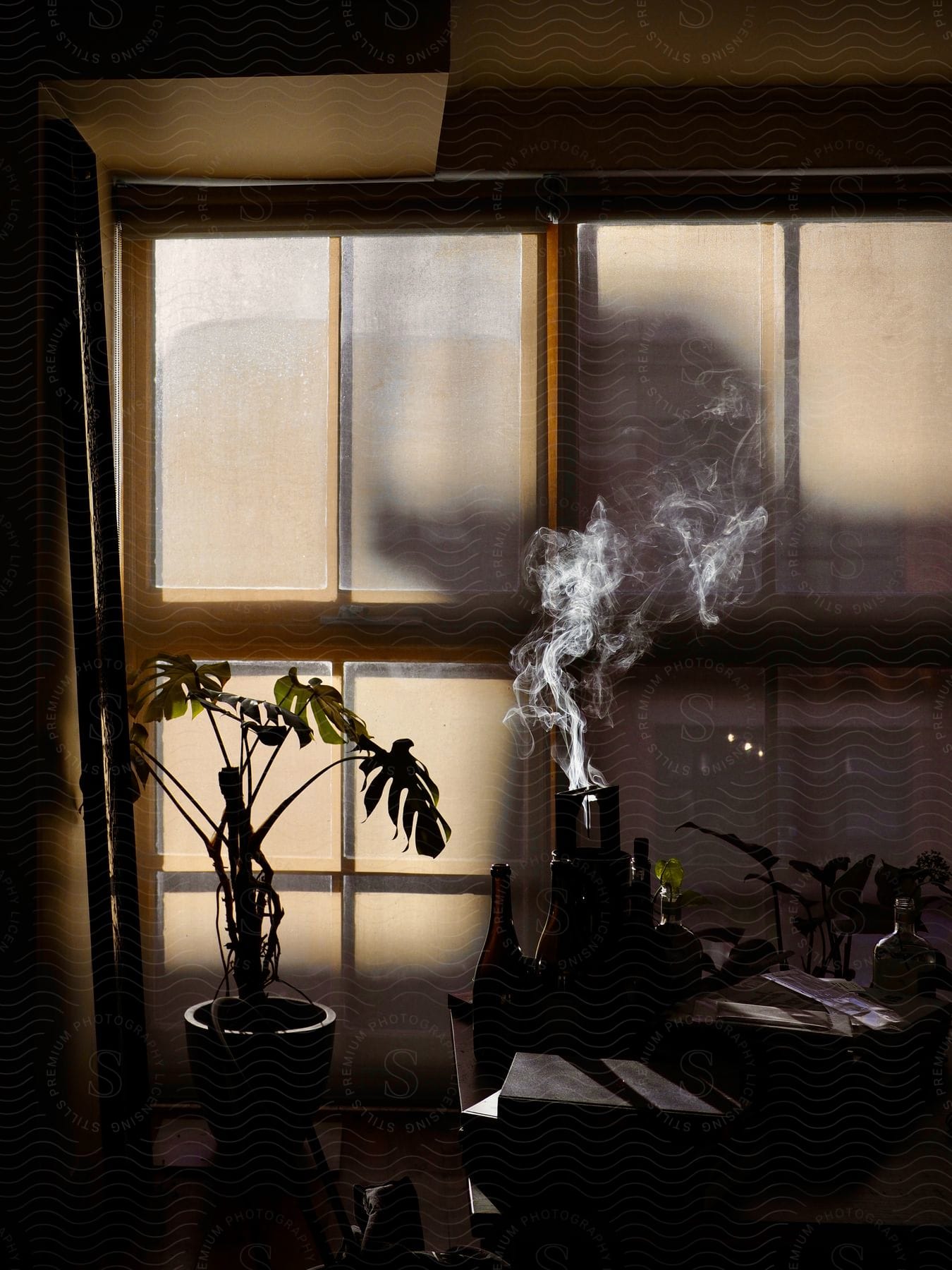 Incense smoke rising from one of several bottles on a table near a large window