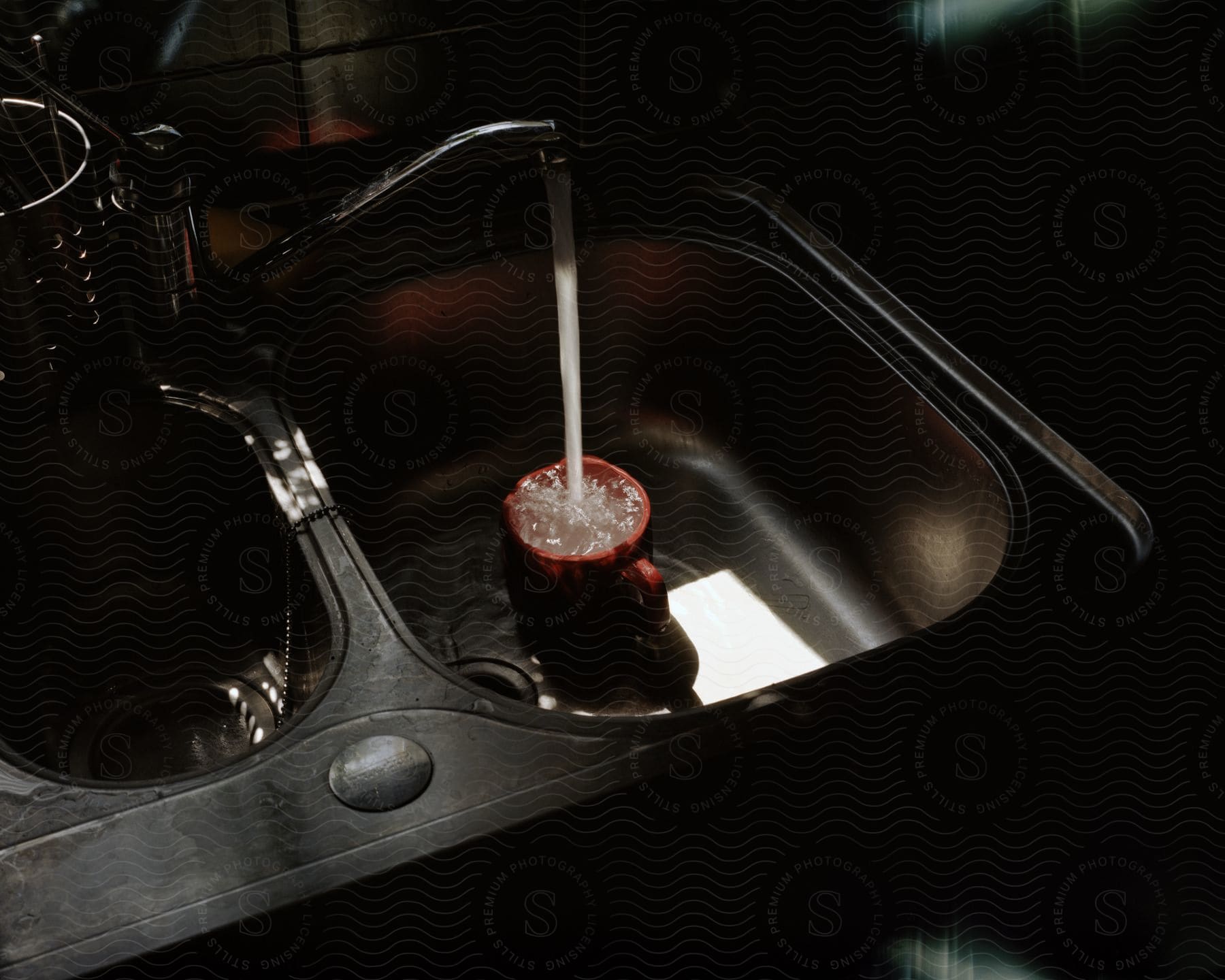 A faucet filling up a cup in a stainless steel sink.