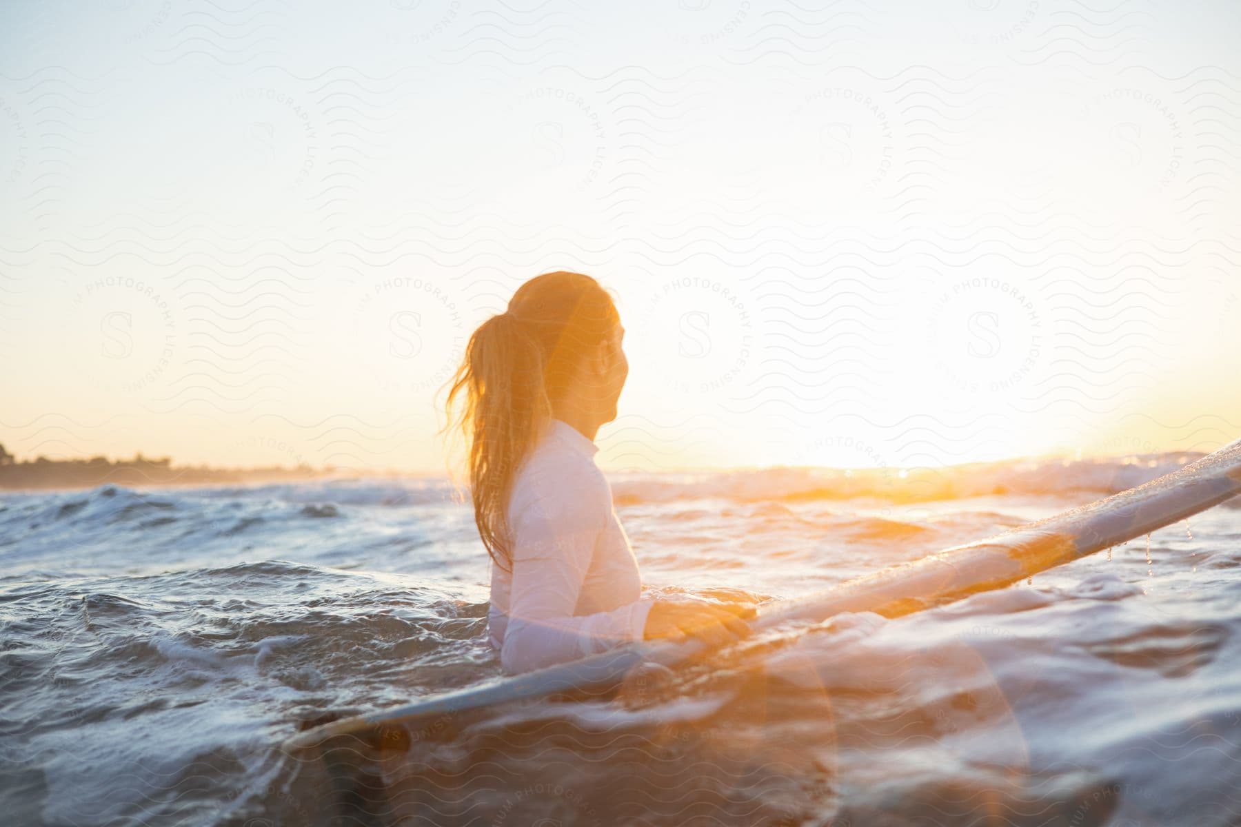 Woman in water at sunrise with surfboard.