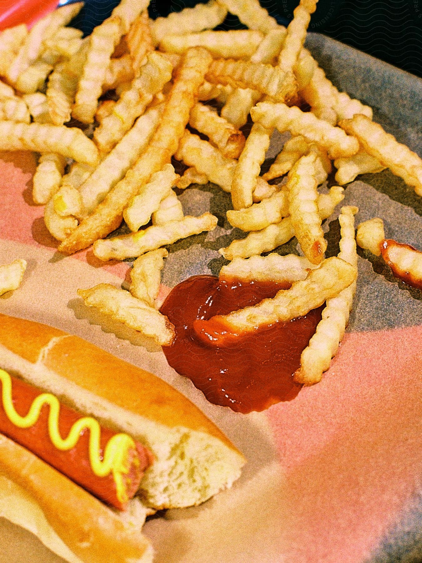 Crispy French fries with ketchup and a hot dog with mustard on a tray.