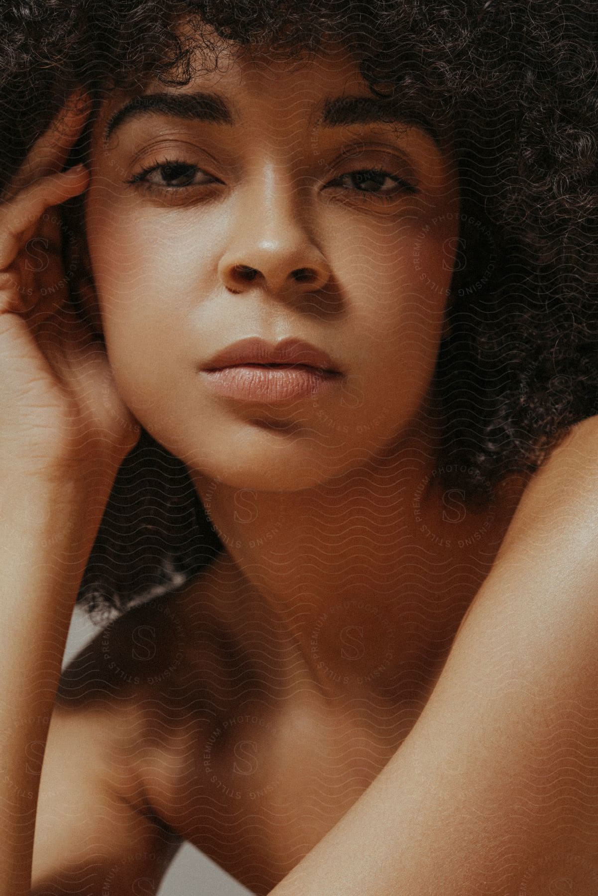 Close up of a woman with curly hair resting her head on her hand.