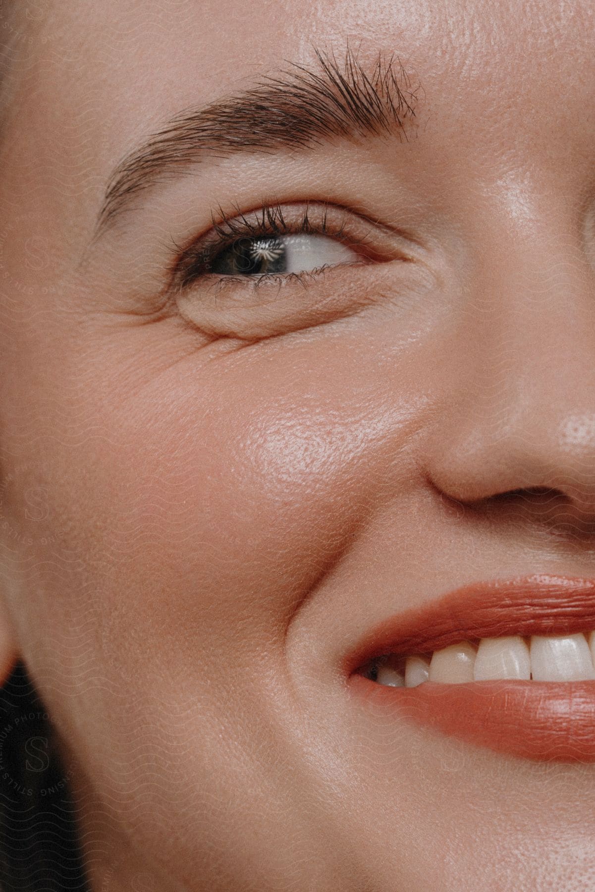 Close-up of a smiling woman's face showing one eye, eyebrow, and her smile, with a clear view of her skin texture.