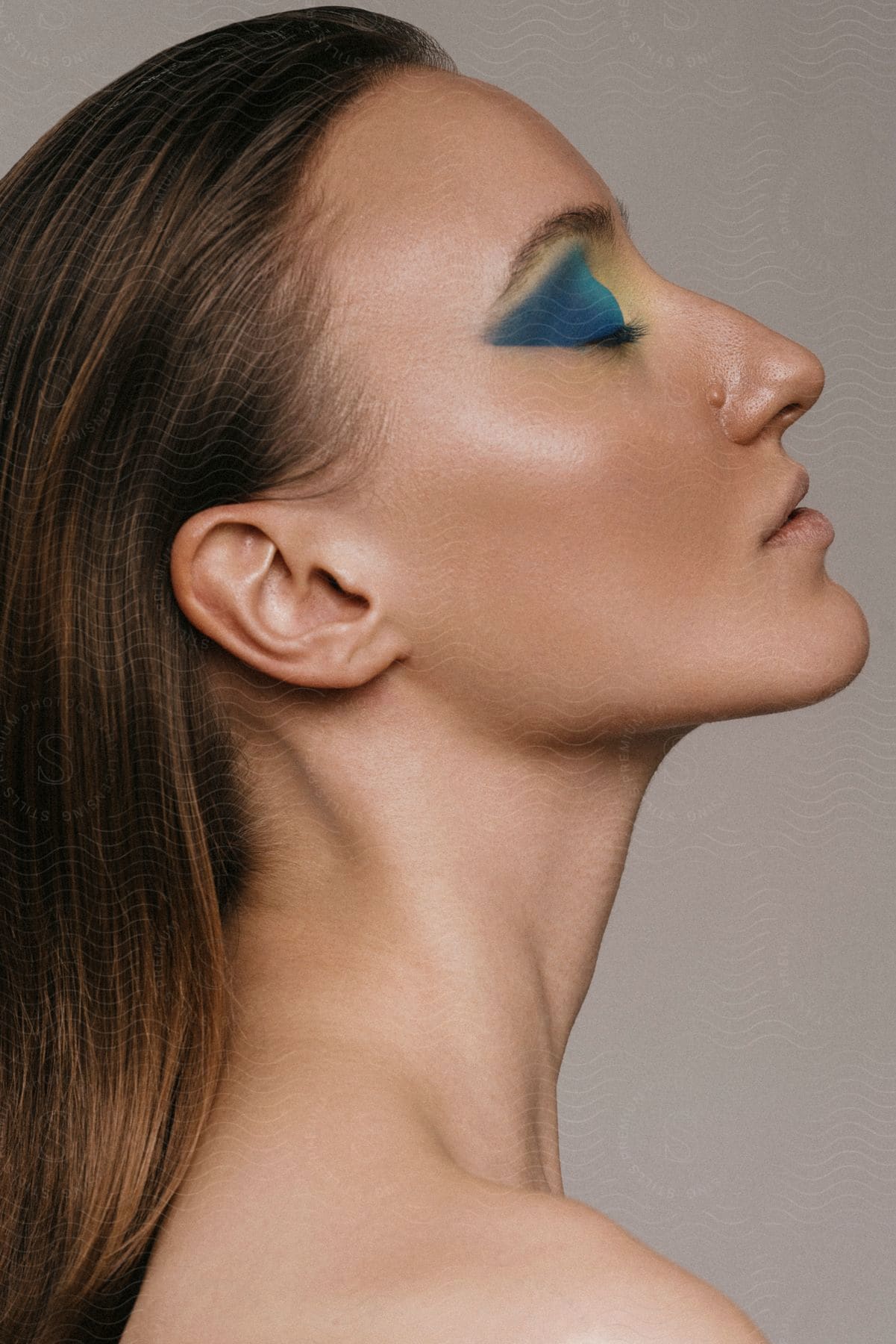 The profile of a woman's face with her eyes closed and blue eyeshadow makeup on her eyes