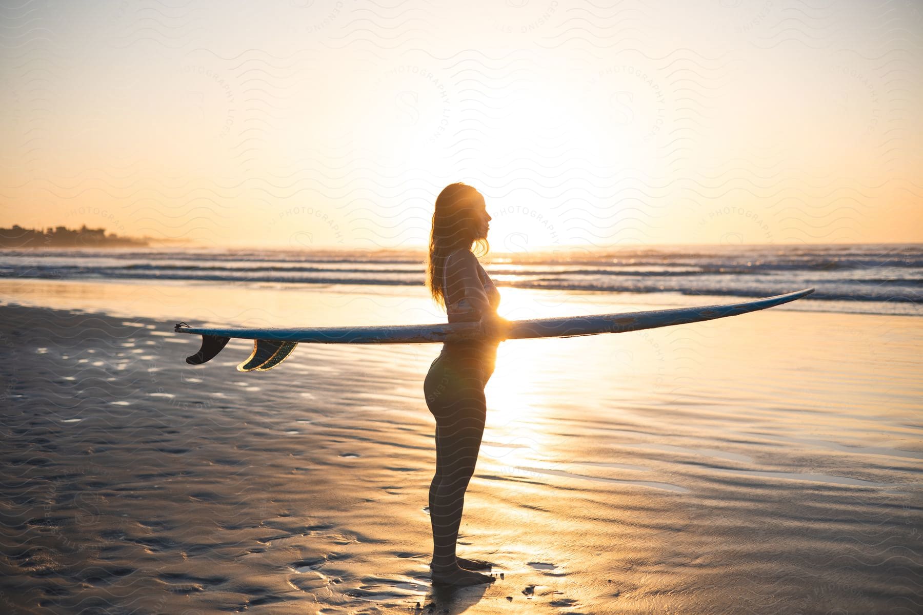 A woman standing at the edge of the ocean holding a surfboard