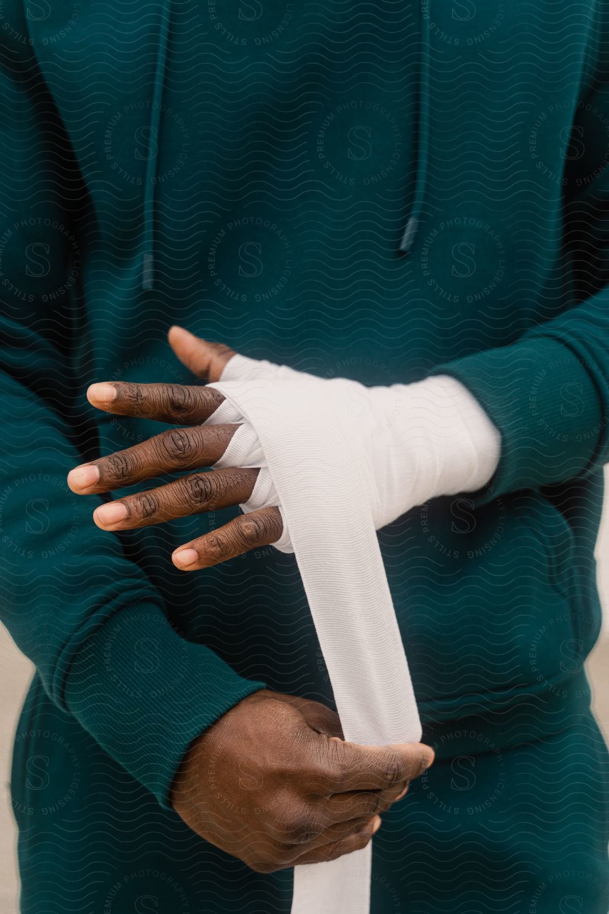 Man wears a sweatshirt and is bandaging one of his hands with a white bandage.