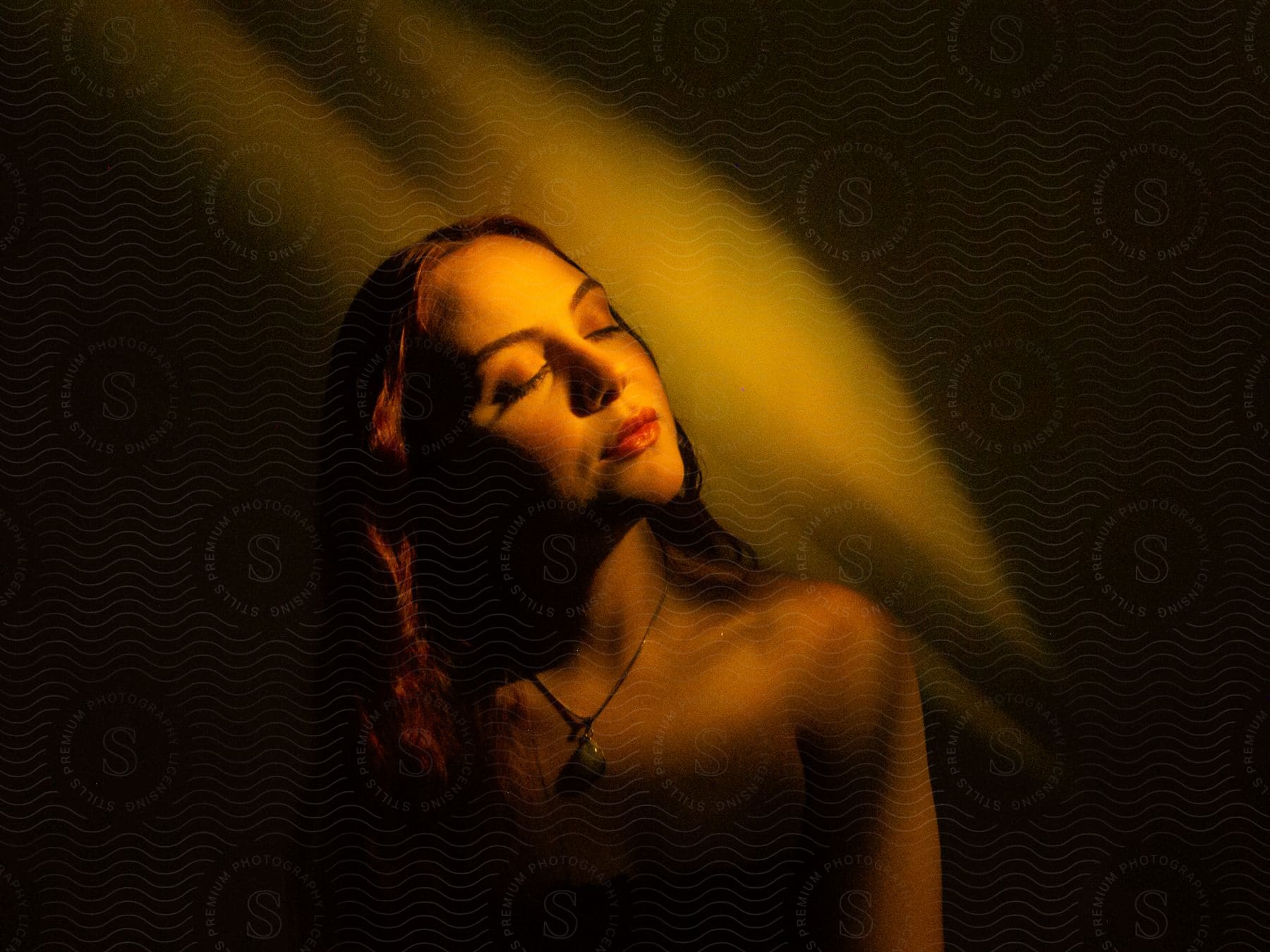 Portrait of a young woman with her eyes closed wearing a necklace and the reflection of light on her face