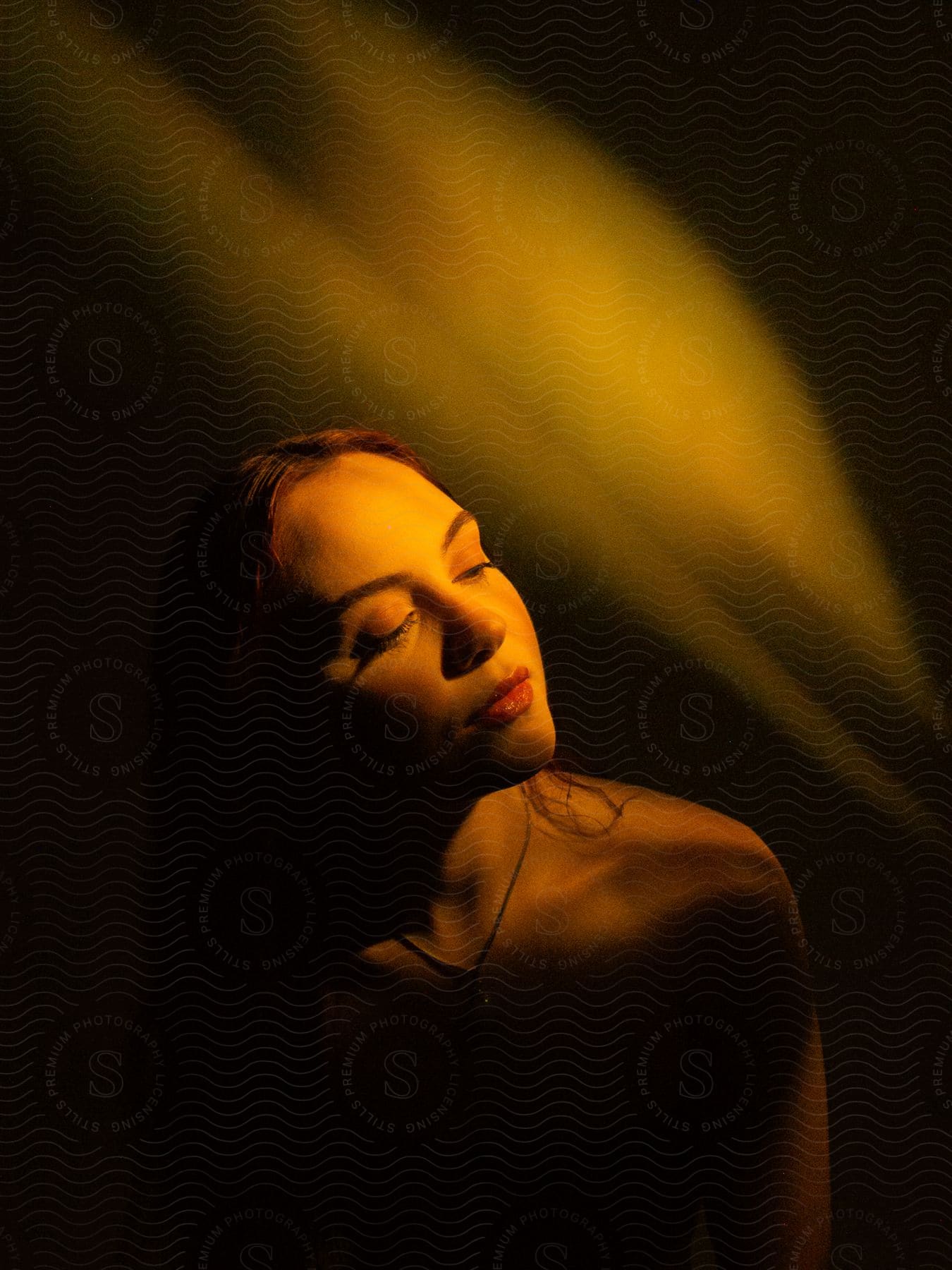 Redhead woman with makeup and red lipstick wearing a necklace and a low beam of light on her face.