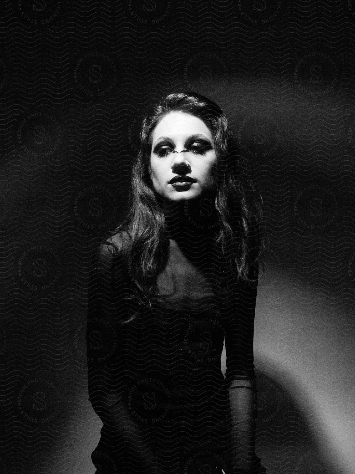 Stock photo of model woman sitting wearing a long-sleeved black dress and makeup.