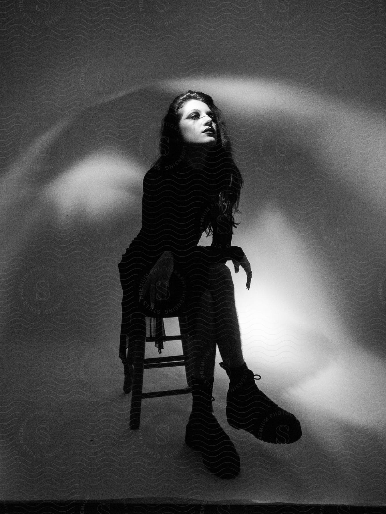 A portrait of a woman who is sitting on a chair and she is looking to her left in black and white tones