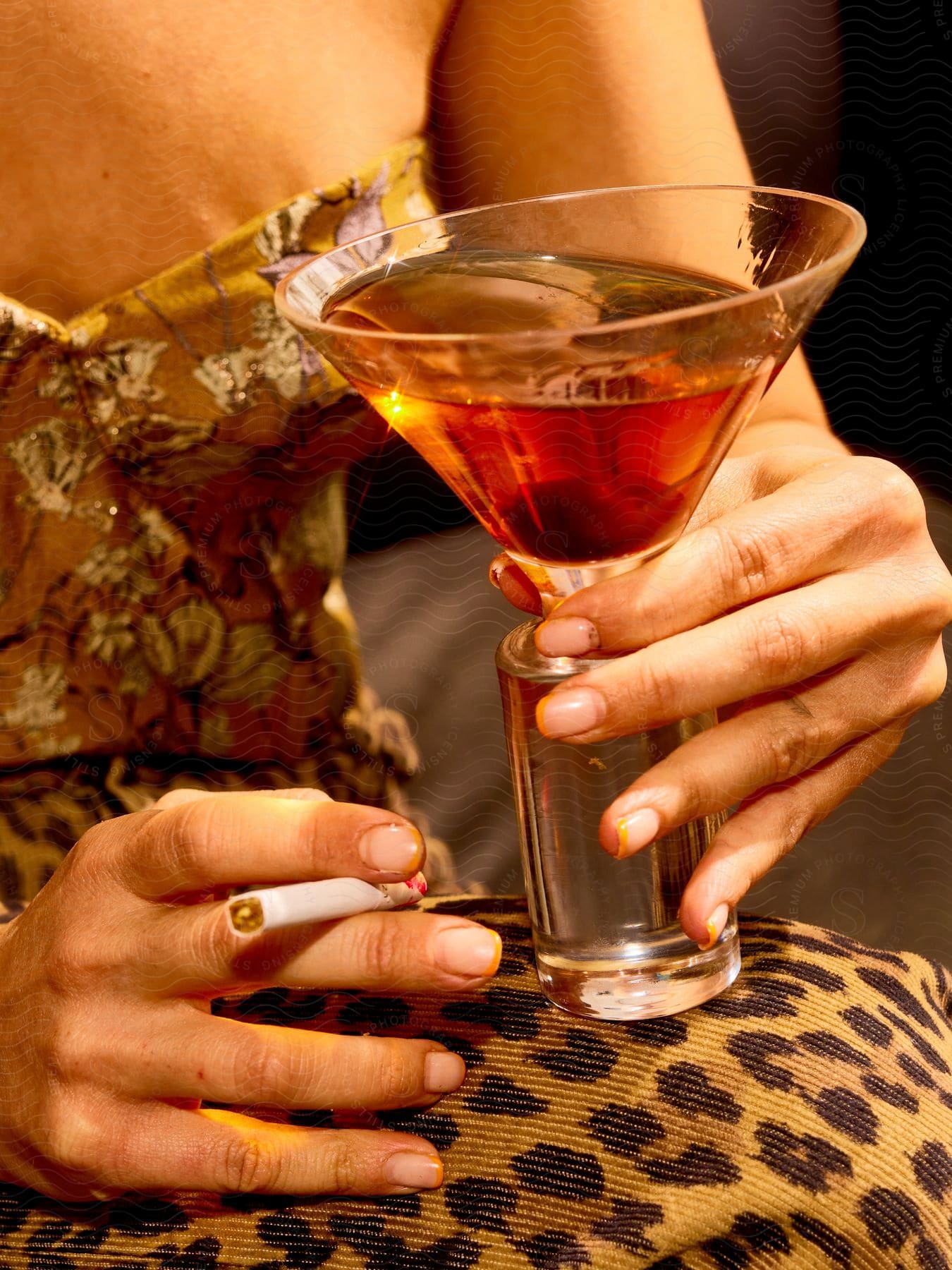 Stock photo of a person holding a martini glass with amber liquid and a cigarette