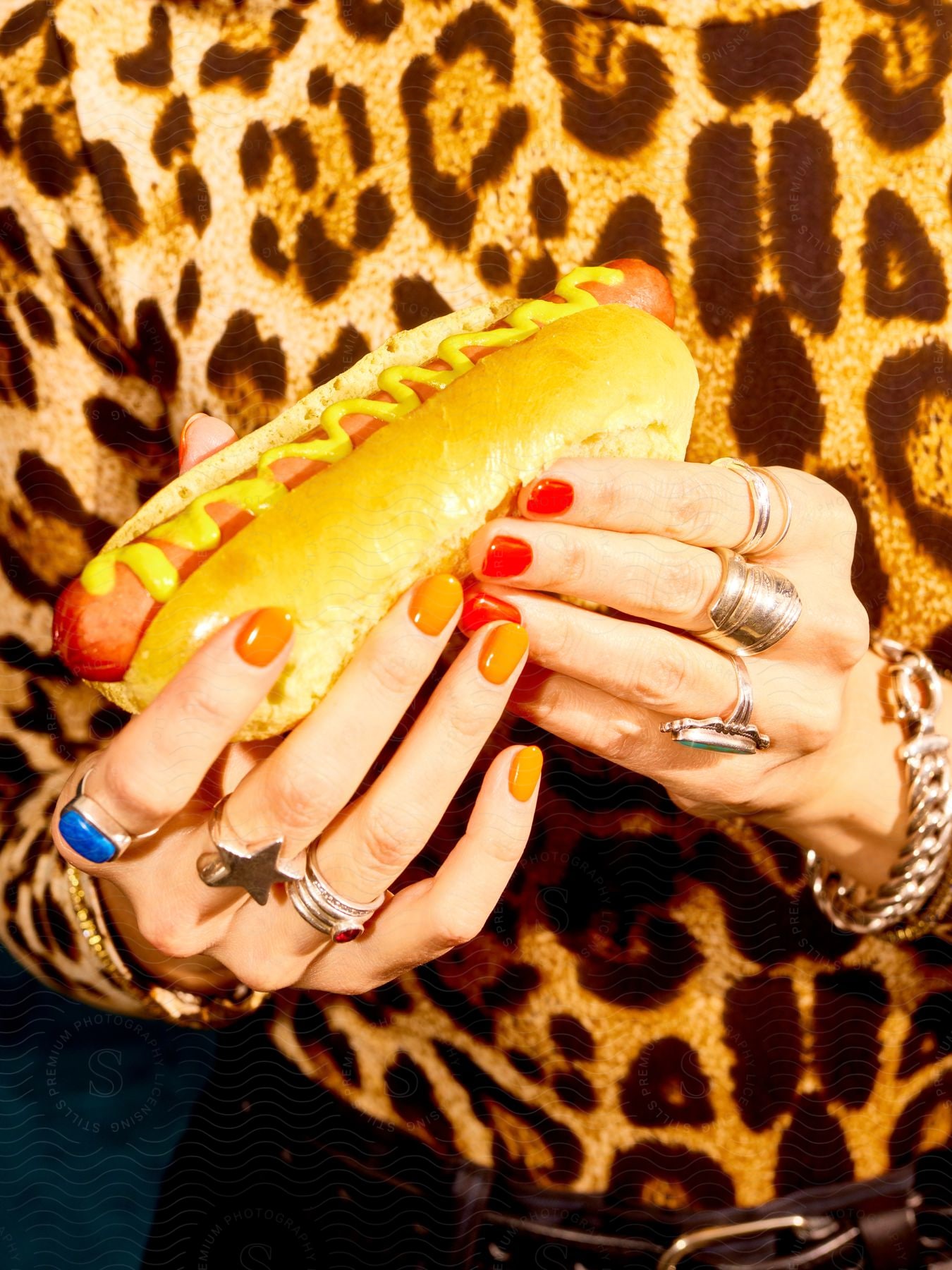 Hands of a person with colored nails holding a hot dog in contrast to the person's yellow and black clothing