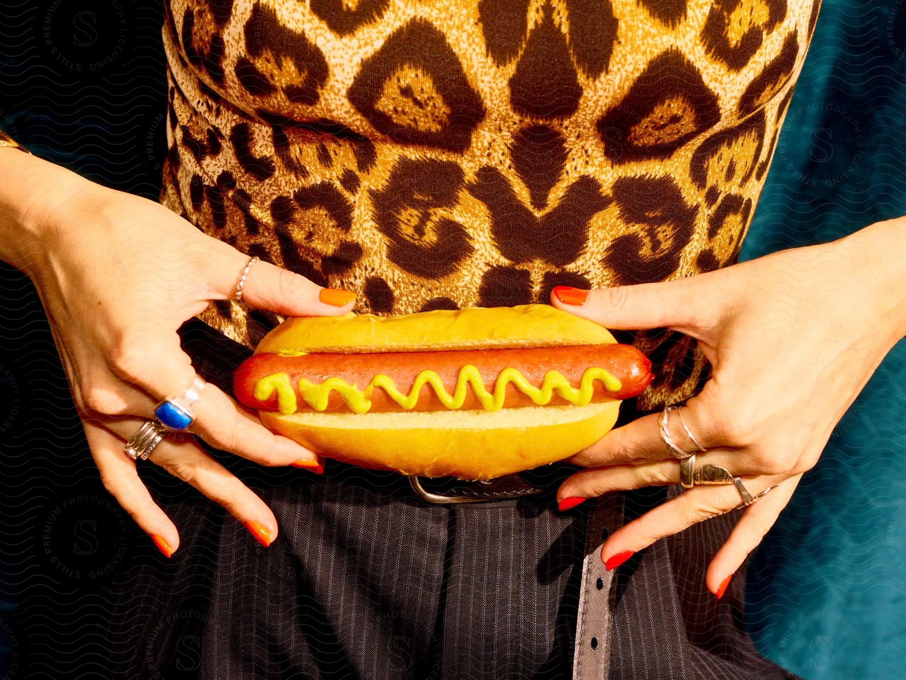 Two female hands holding a hot dog against a leopard print fabric background.