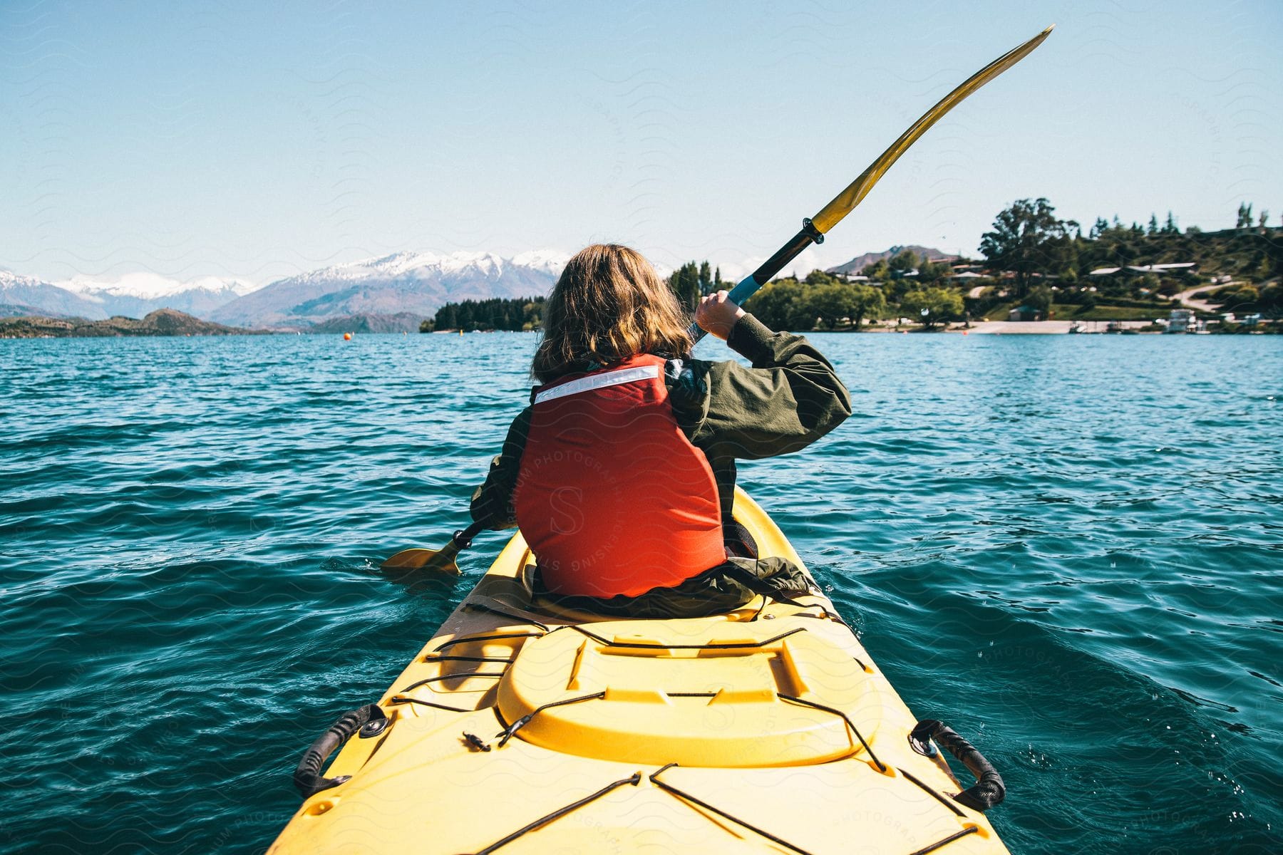 A person with long hair a green jacket and a red lifejacket kayaking over a sea