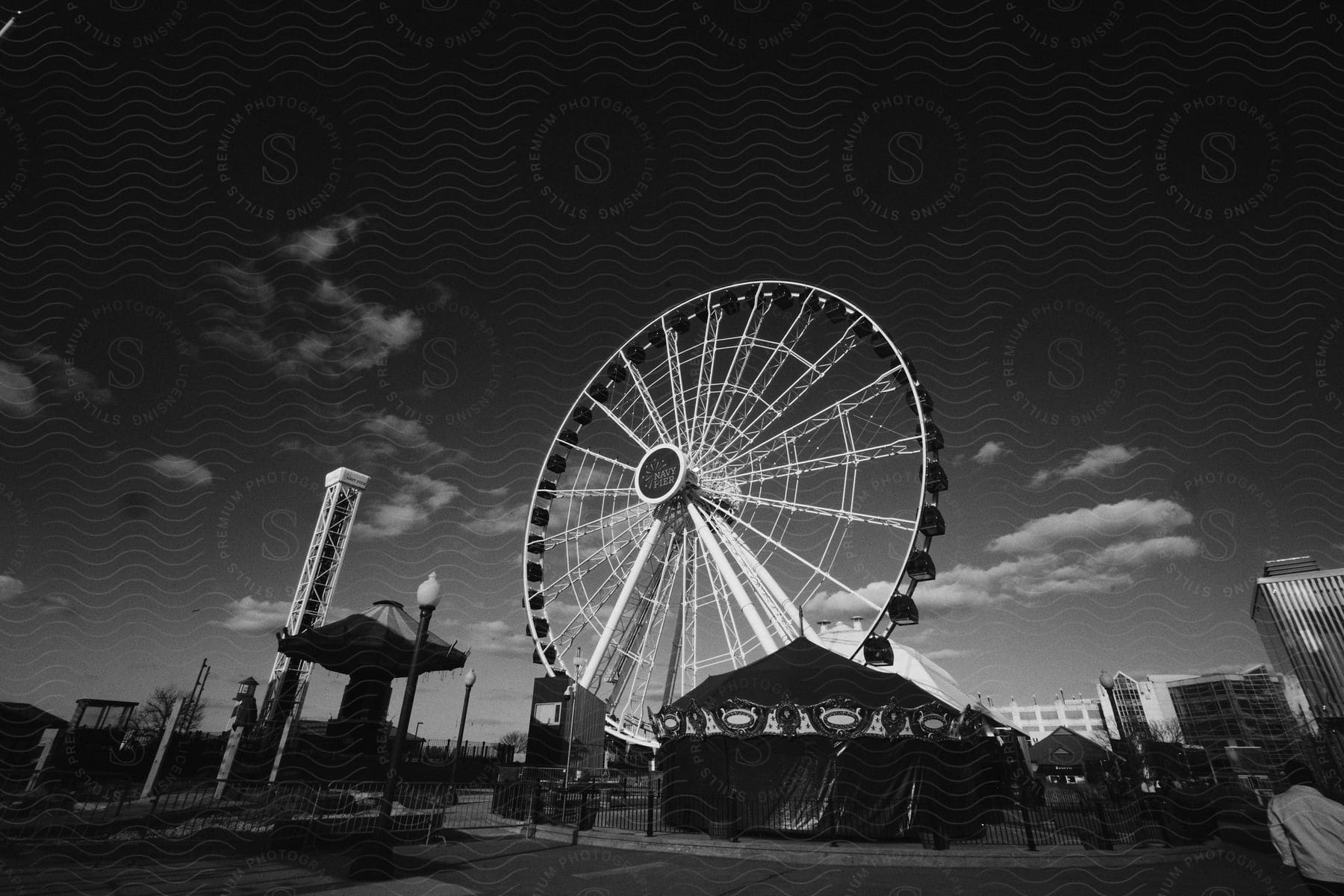 A man walking toward an empty amusement park with a large ferris wheel under a dark sky.