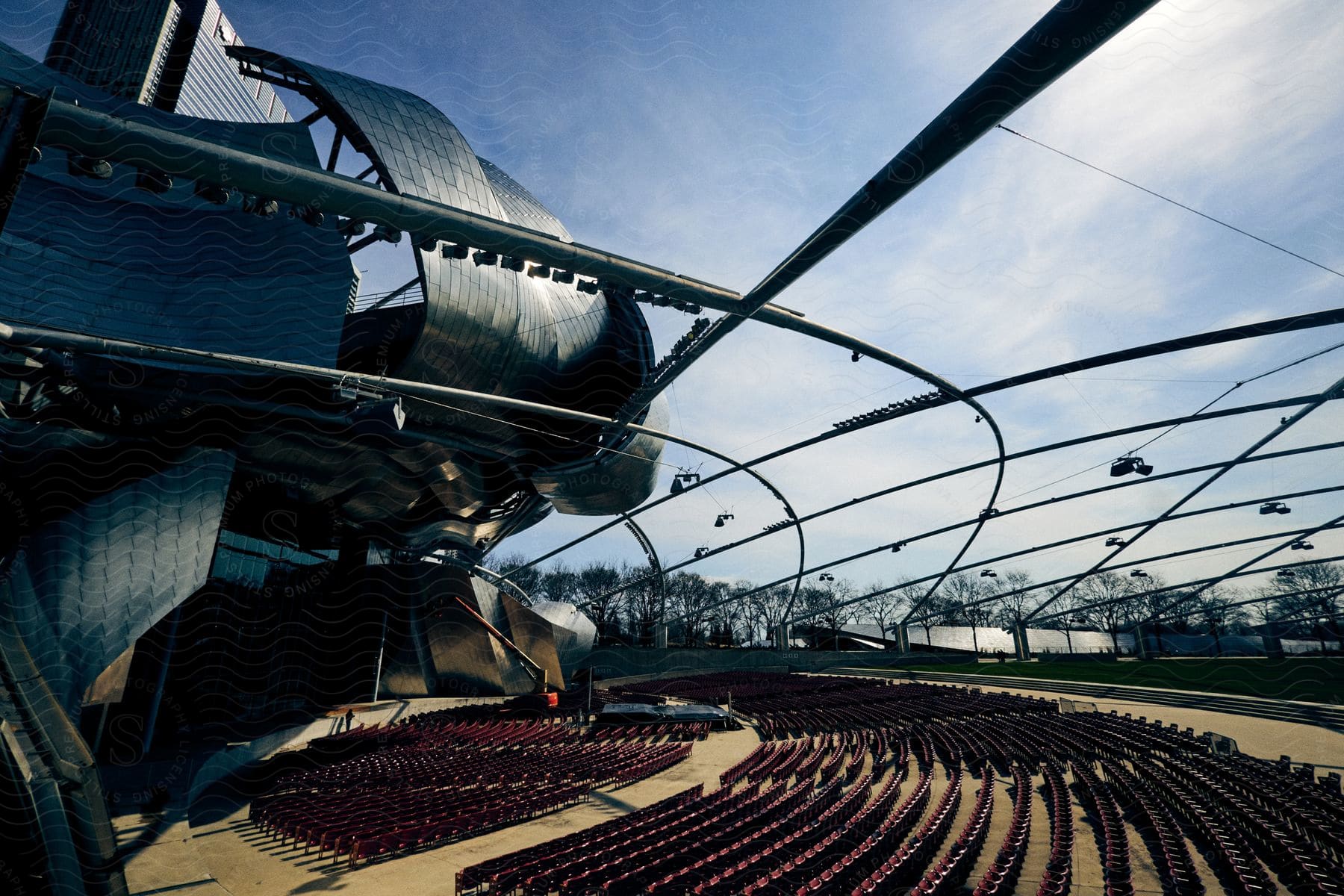 Modern architecture of the Jay Pritzker Pavilion theater with red chairs during the day.