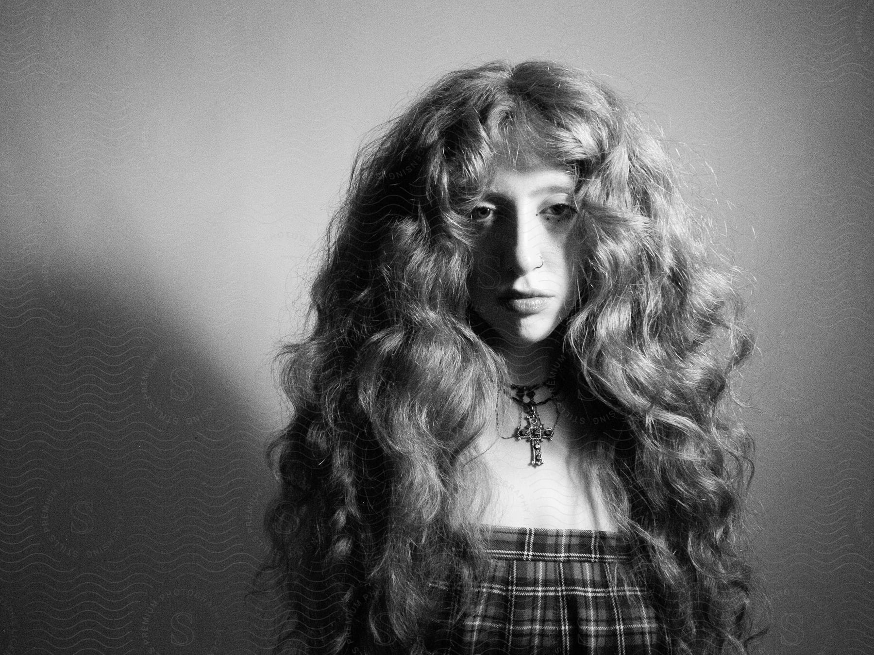 A woman with very long and very curly hair looks directly at the camera as she is posing.