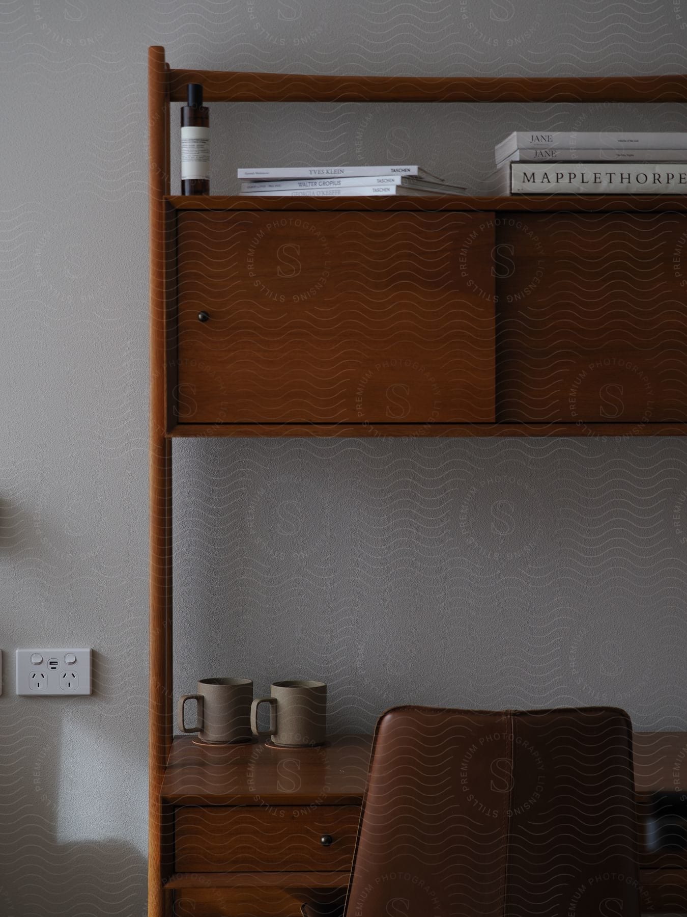 A wooden desk with a panel door shelf above and books artfully stacked