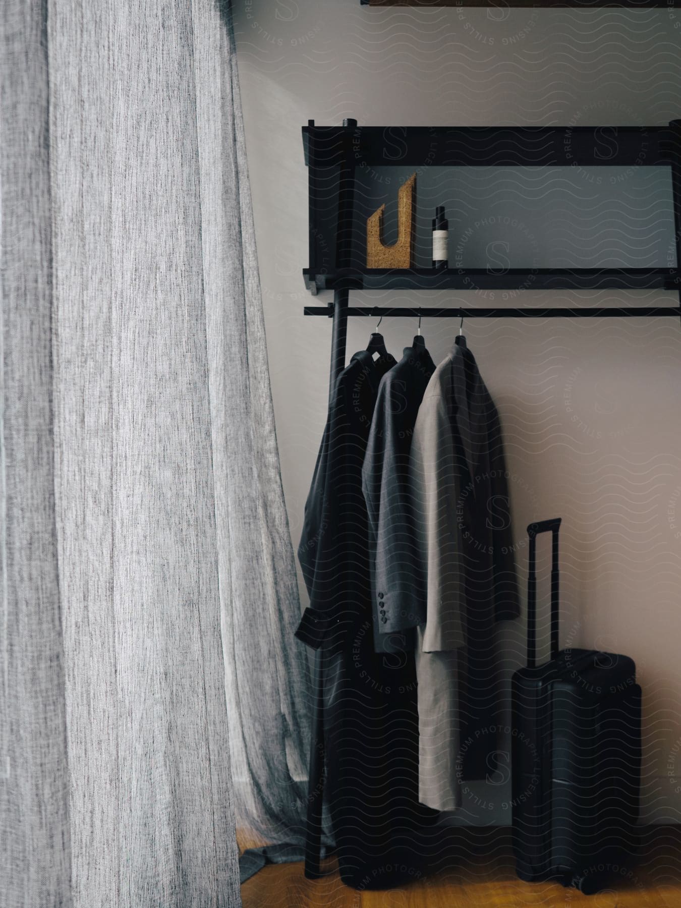 Blazers, jackets and a suitcase on hangers in a room next to the window with curtain