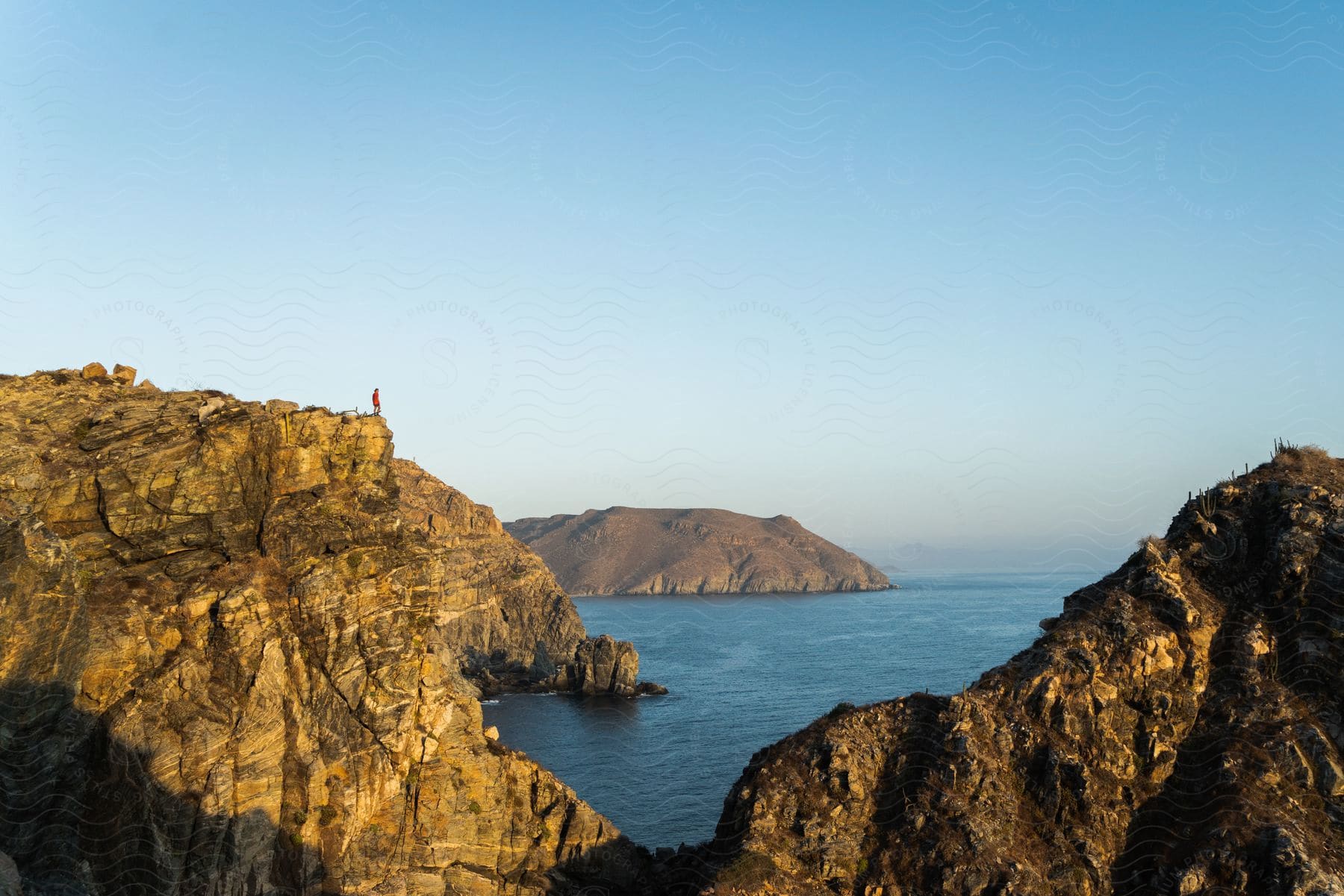 Person standing on a promontory overlooking the water and rocky terrain