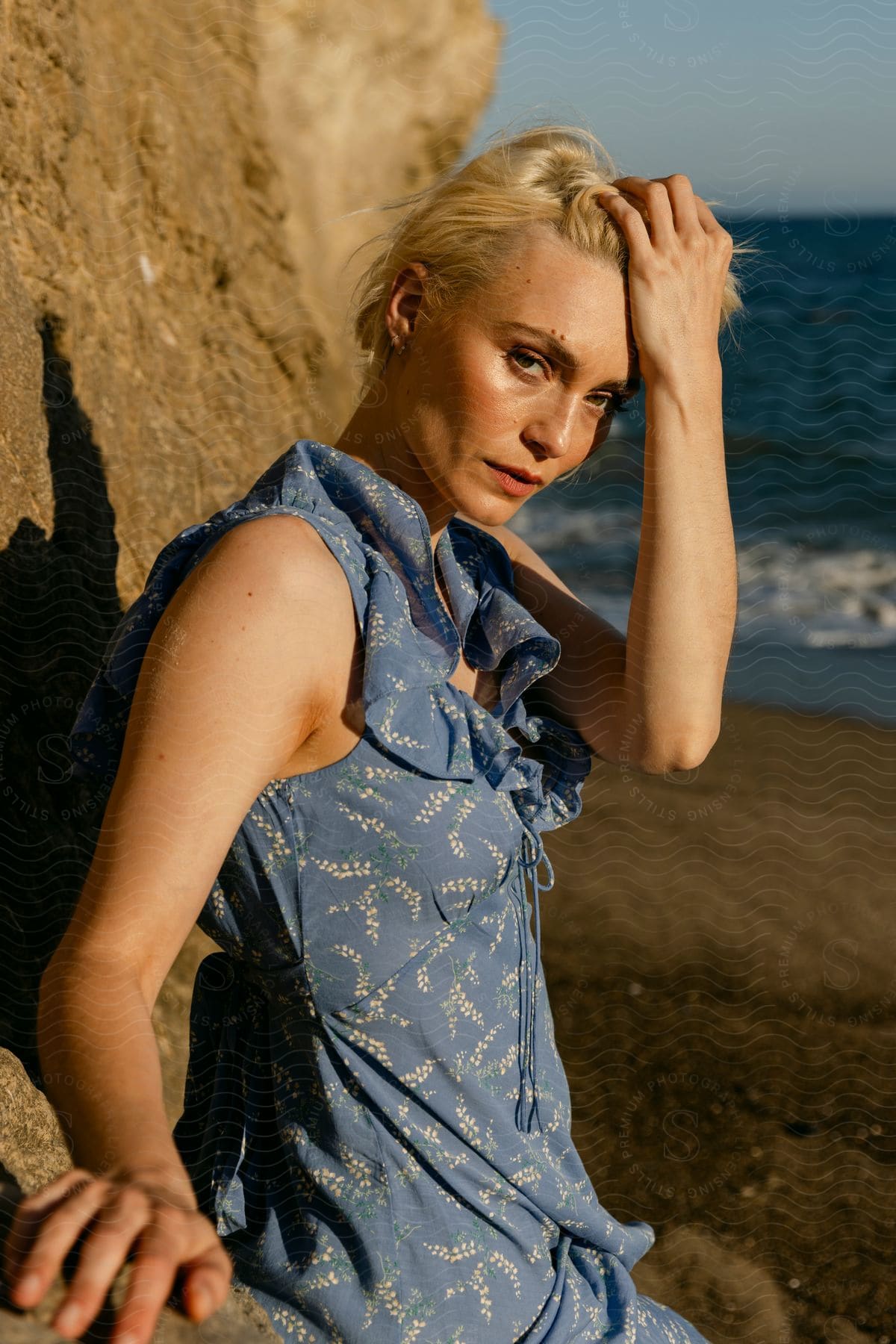 A woman with blonde hair wearing a blue dress with a floral pattern reclined on a cliff