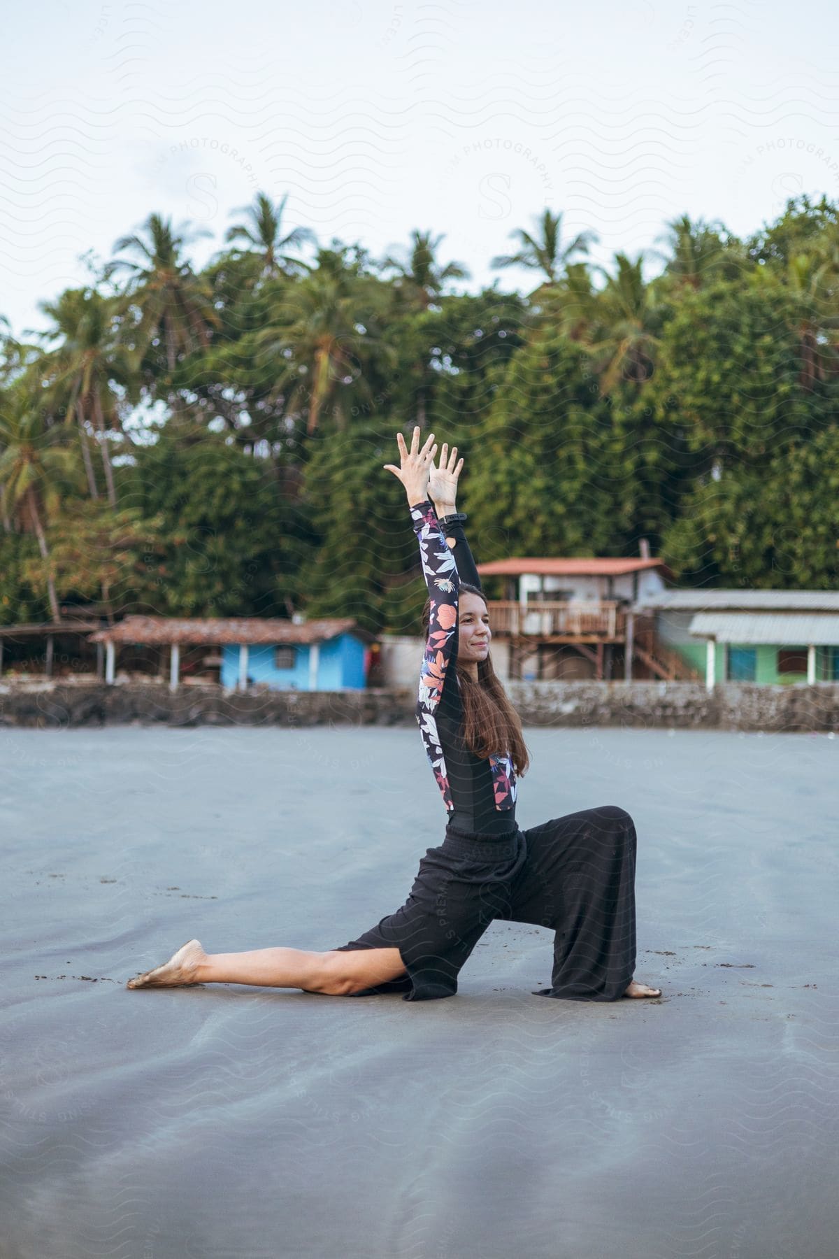 Woman with arms in the air and on one knee doing stretching exercises on the beach