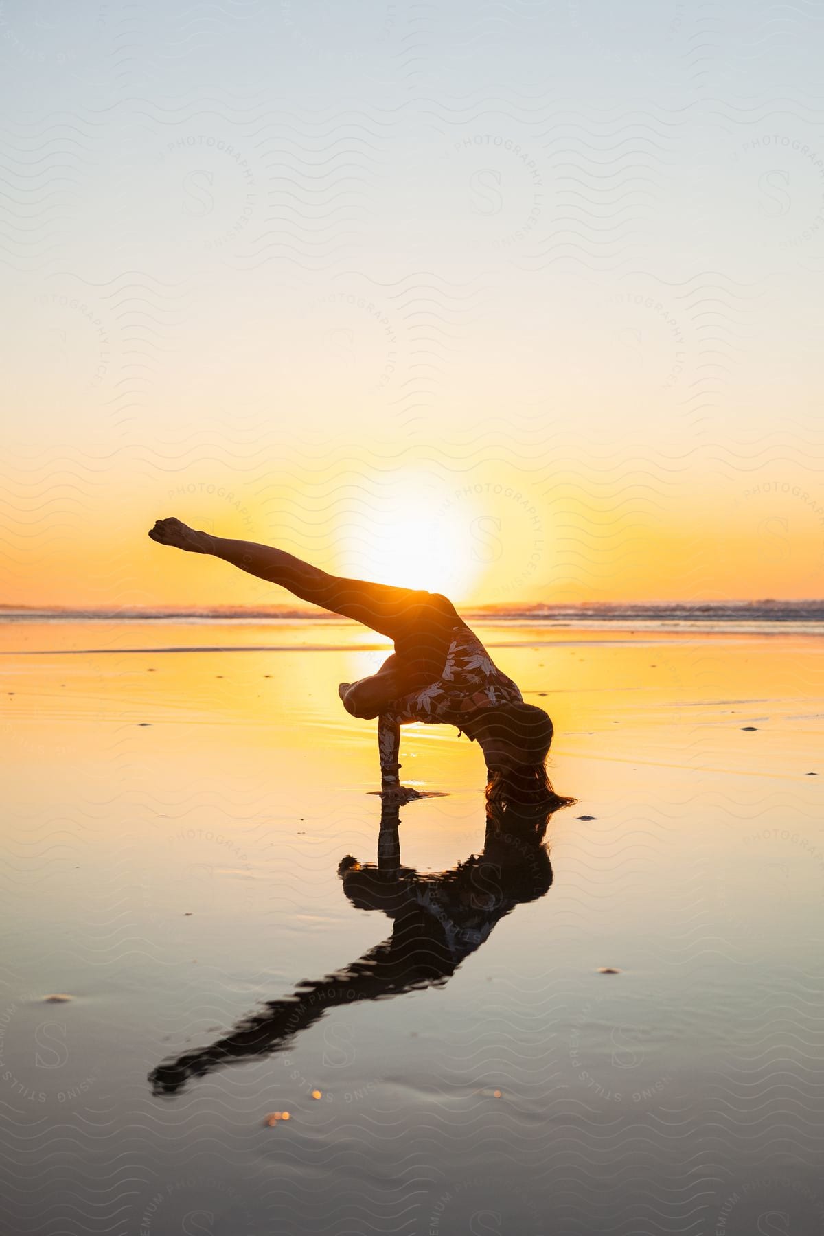 A person practicing yoga on the beach during sunset. The person is in a balancing pose, with one arm and one leg extended, creating an elegant form.