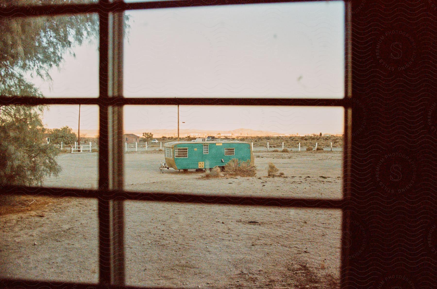 A view through a window reveals a desolate landscape with a lonely old trailer.