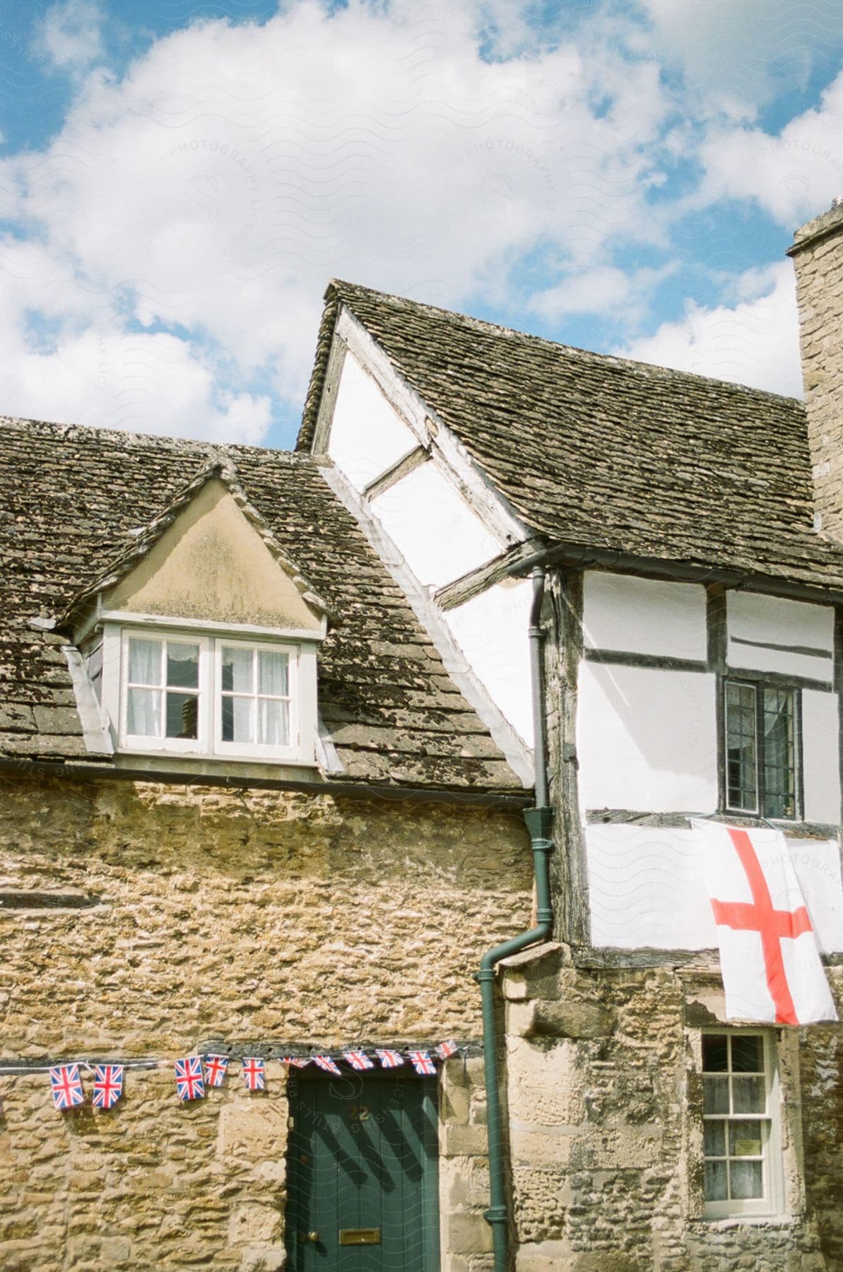 A charming stone house with a thatched roof, adorned with the English flag and small British flags.