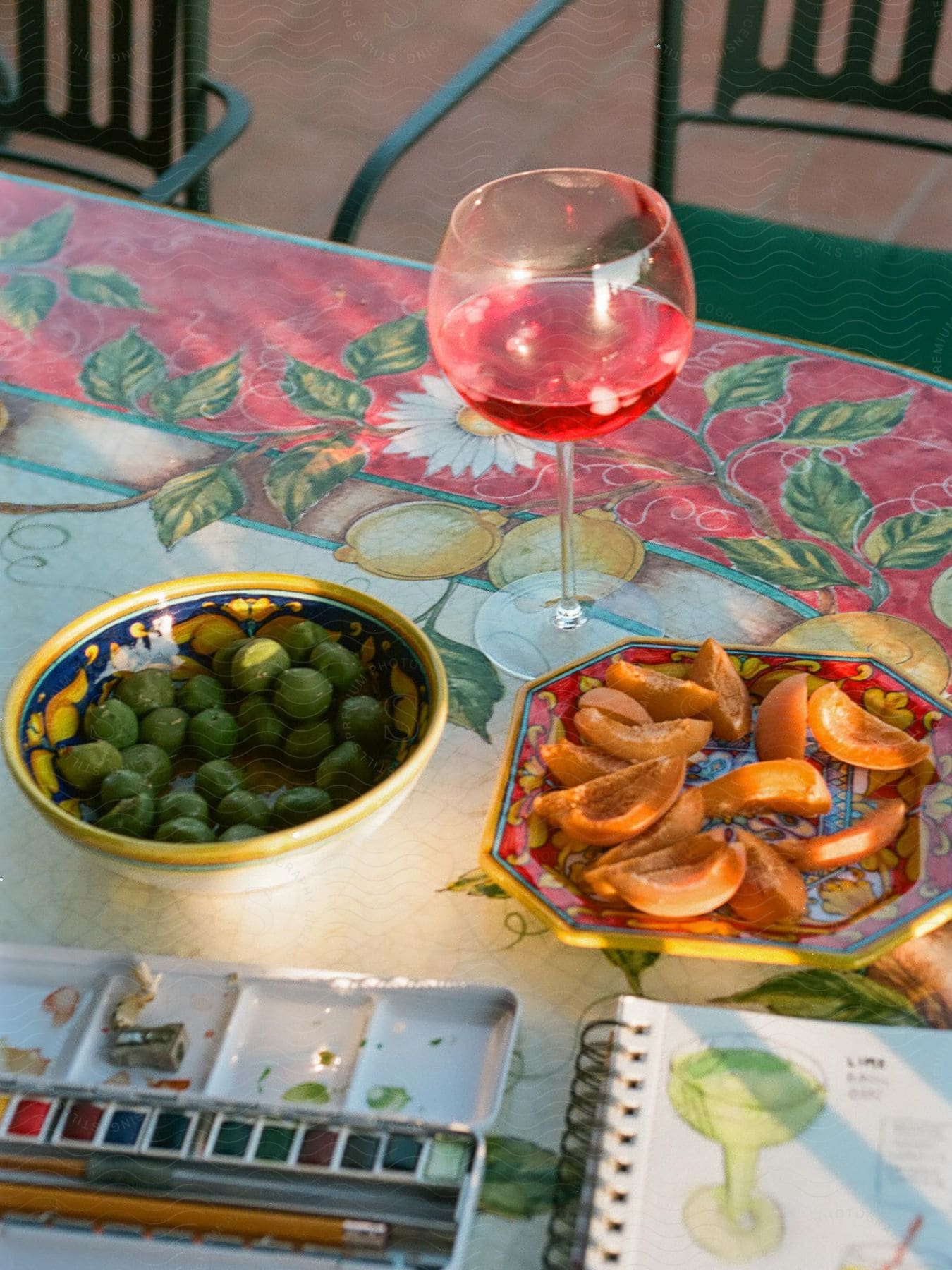 Glass of wine with fruit and olives on a table with watercolor paints and a painting