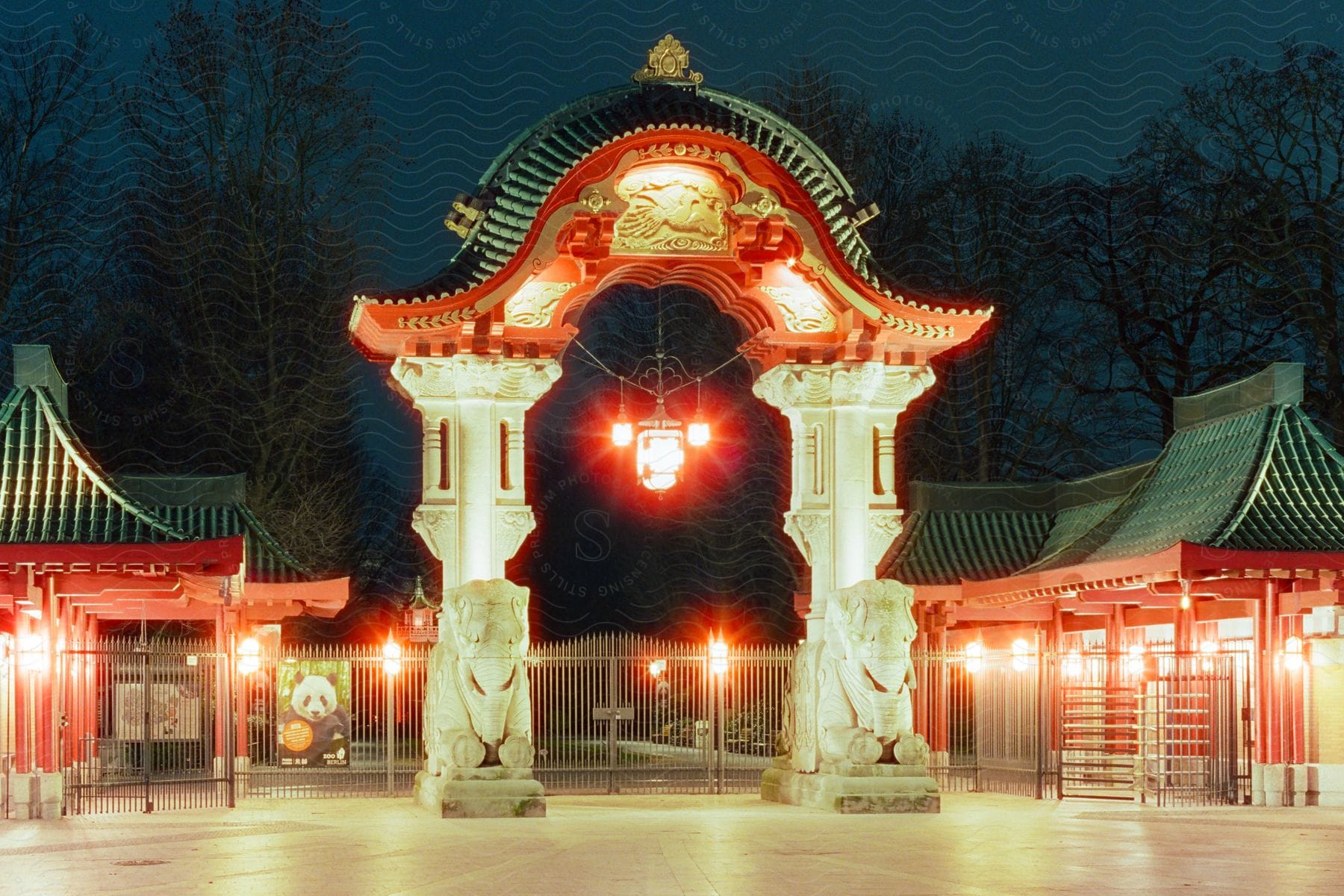 A beautiful traditional Asian-style gate, illuminated at night. Two large stone lions flank the entrance, serving as guardians.