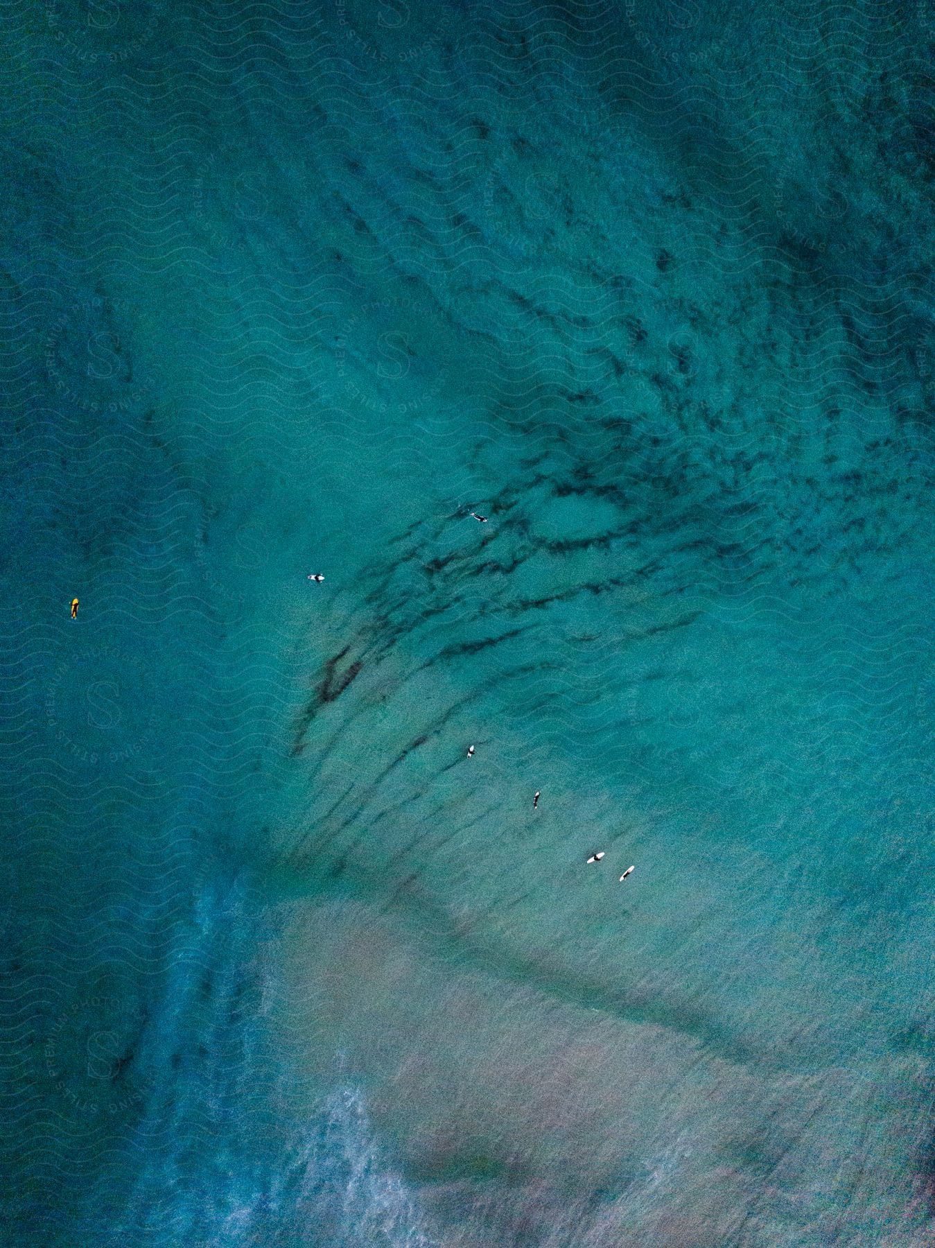 The ocean near the shore with visible sand and people surfing in the water on surfboards.