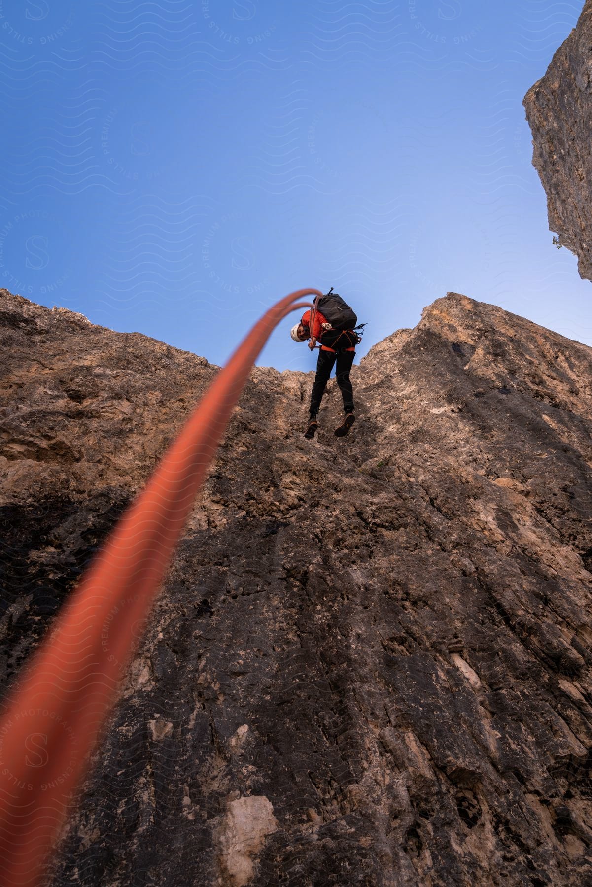 Climber in action descending a steep rock face under a clear cloudless sky.