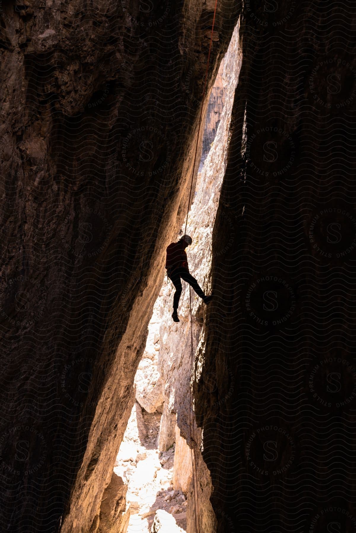 A rock climber hangs on a rope in a narrow cleft between two rock faces.