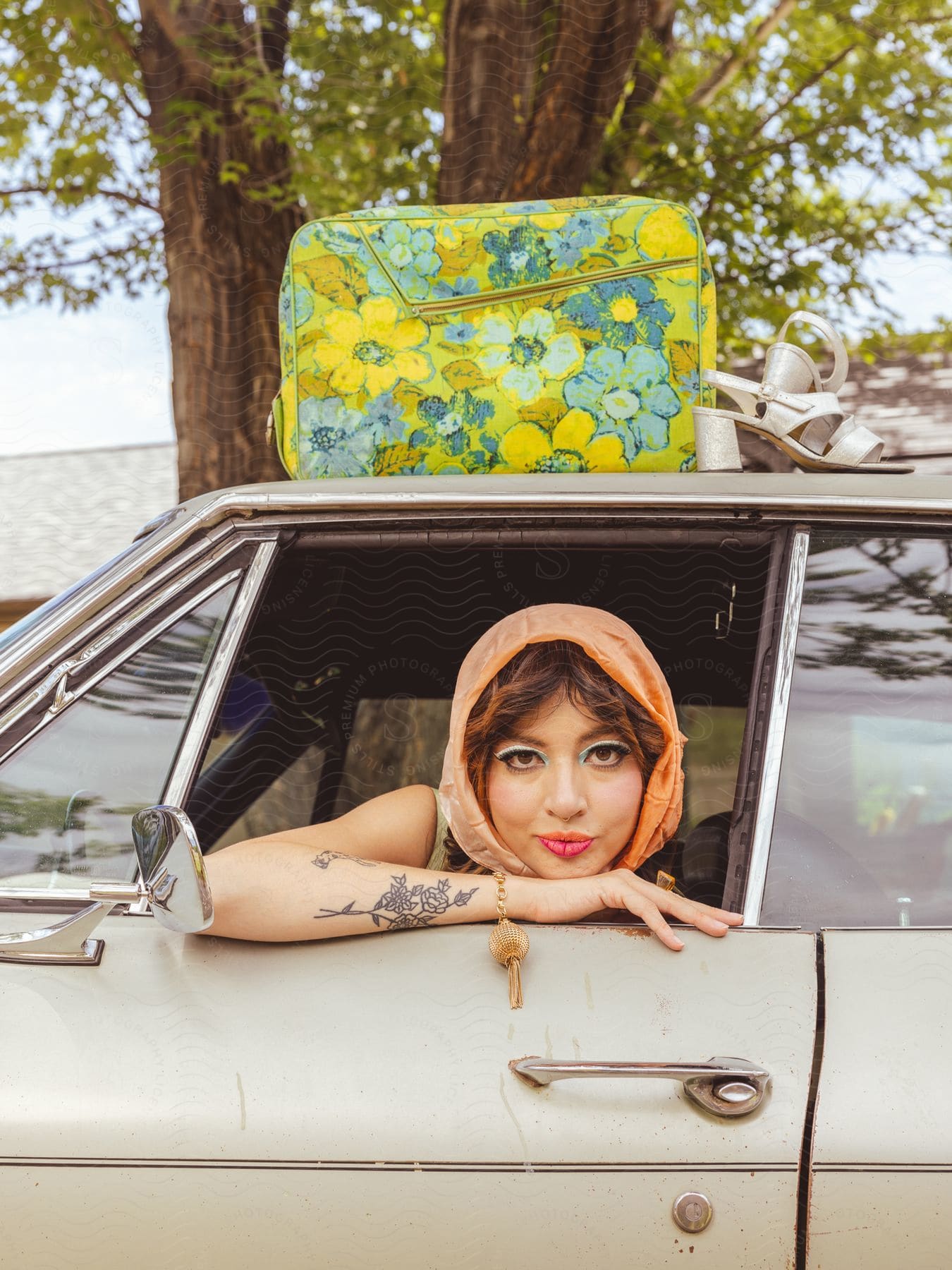 A person sitting in an old car with a floral suitcase on the roof.
