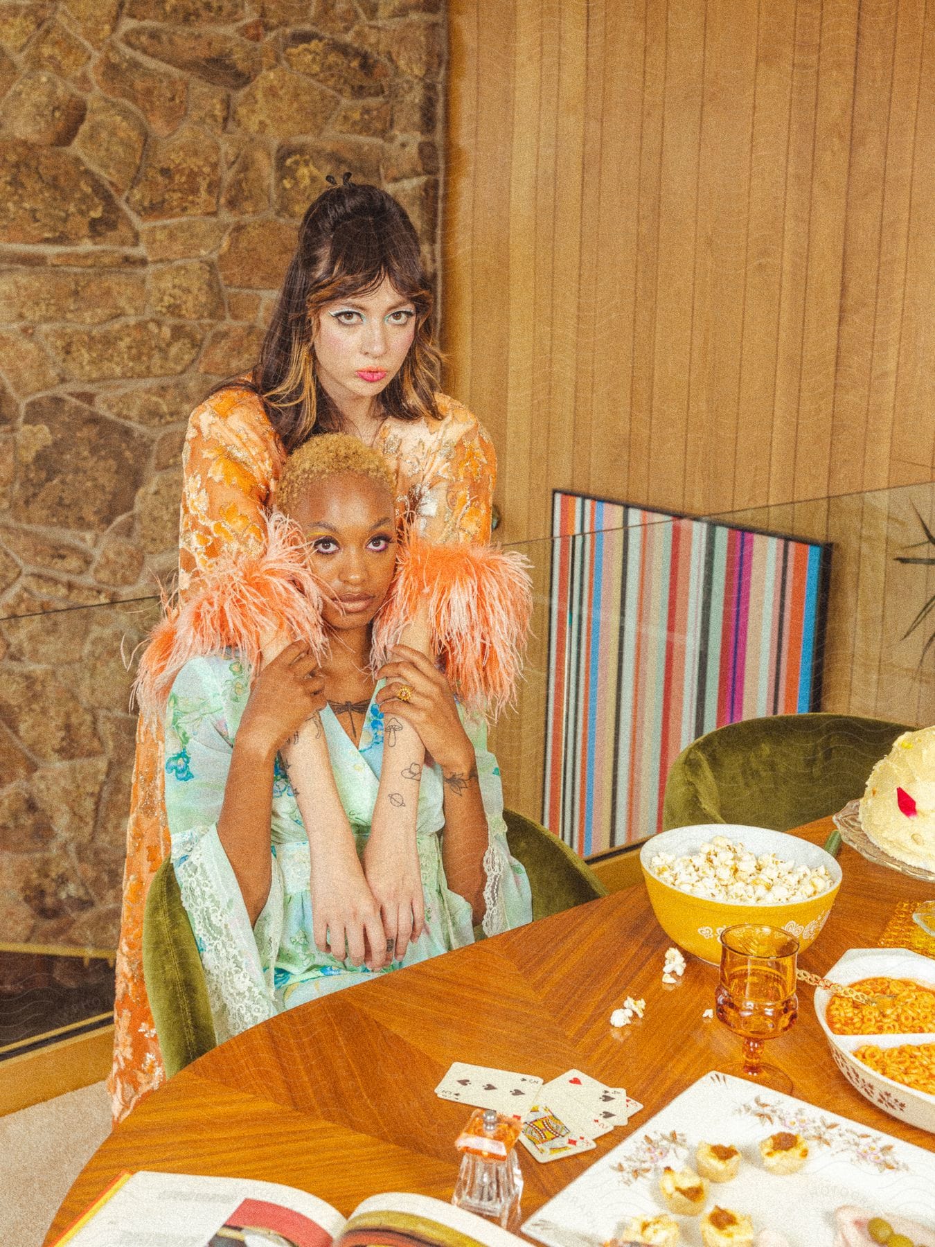 A woman stands behind another woman at a snack and card table.