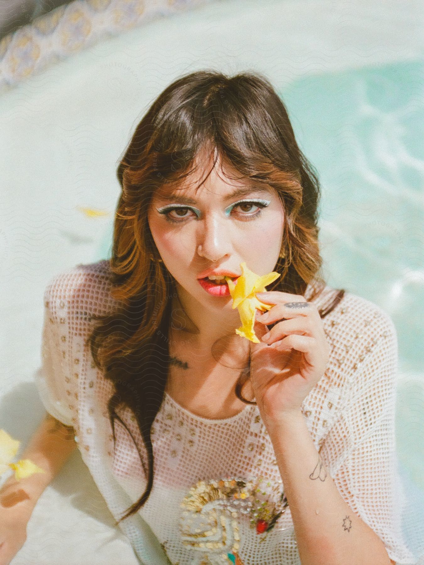 Portrait of a model in the pool with a yellow flower in her mouth and wearing a white dress