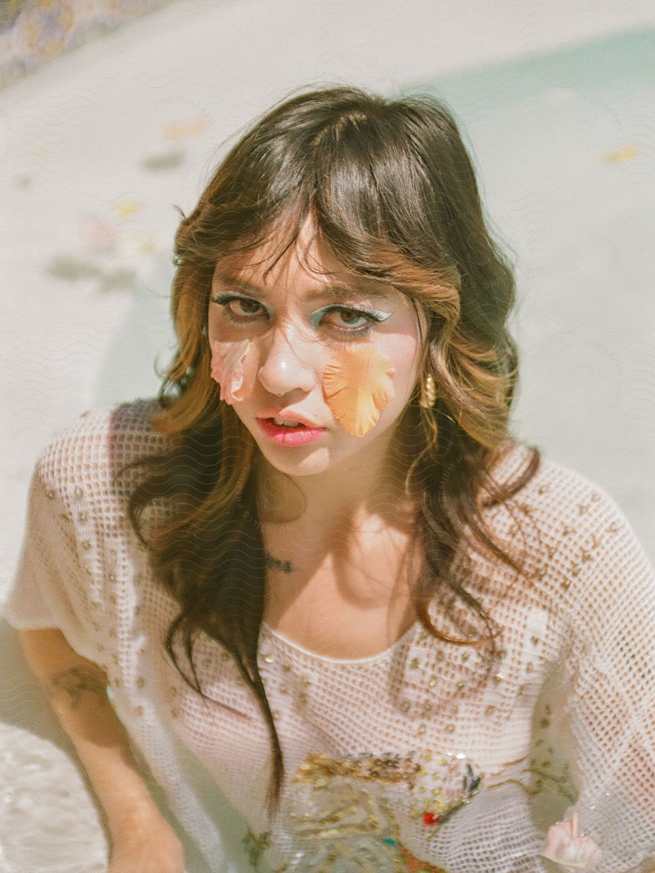 Stock photo of a woman with leaves on her face, wearing a white blouse with intricate patterns.