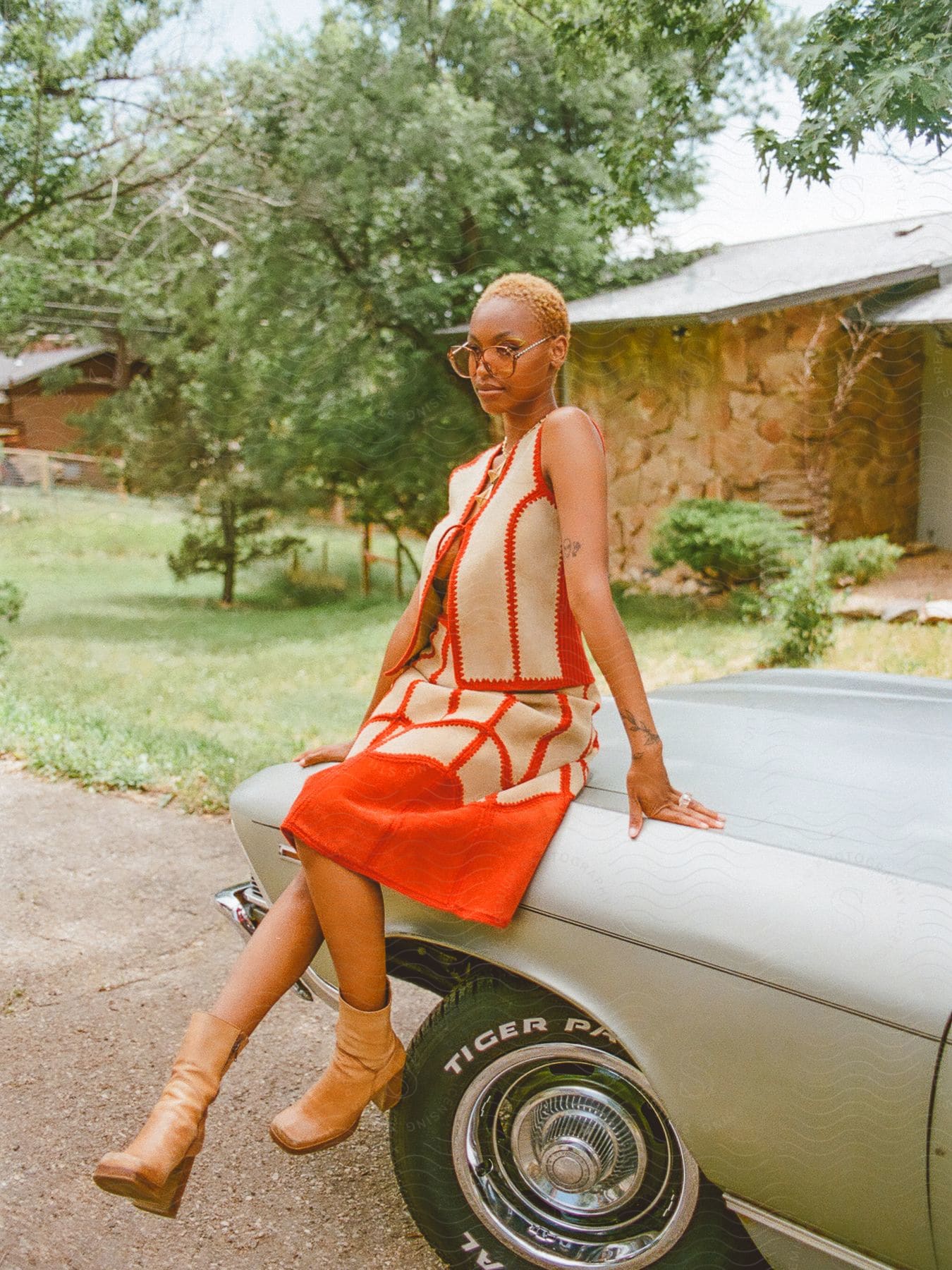 A young black teenager wearing sunglasses poses in front of a car.