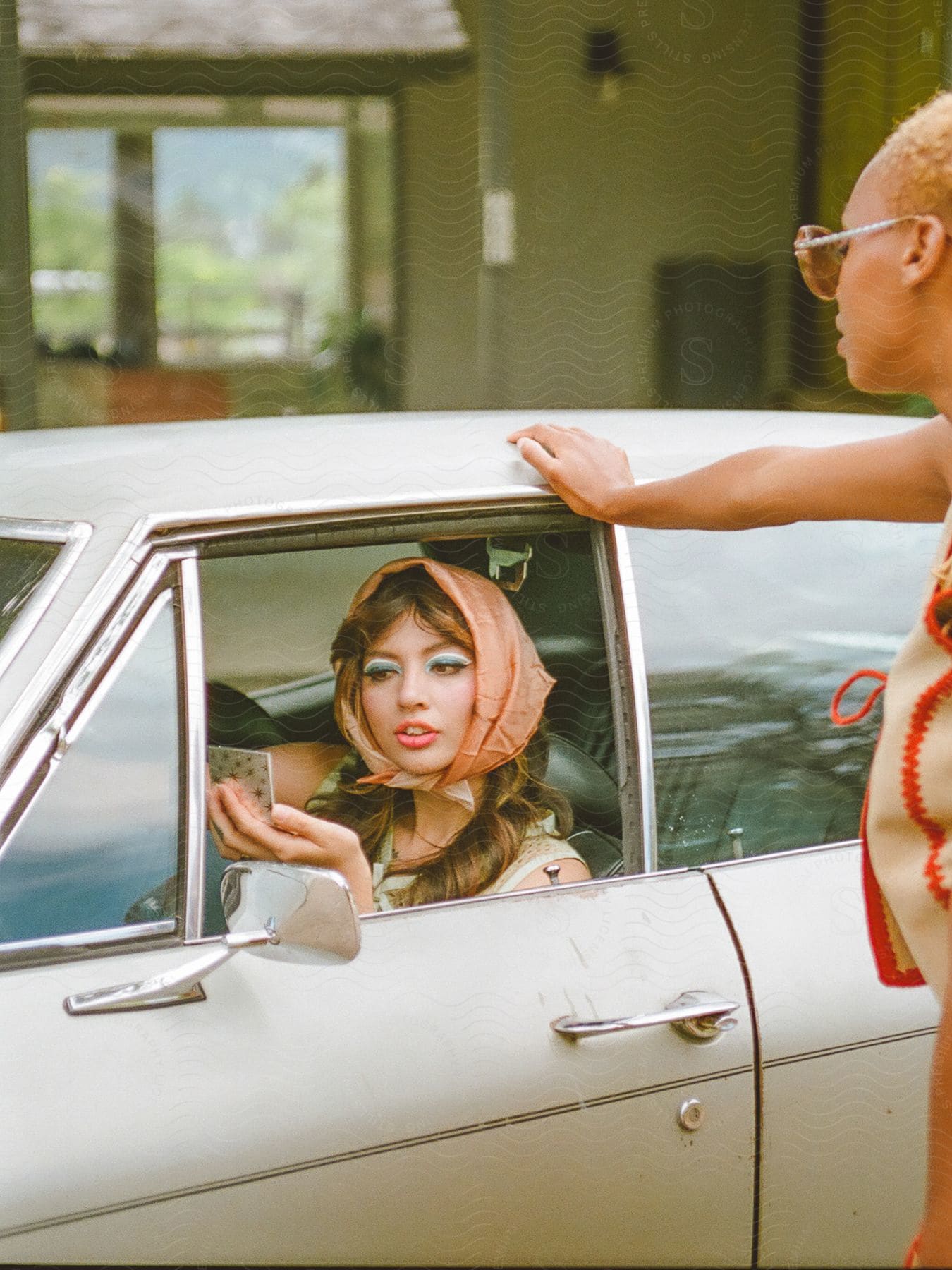 Stock photo of two people, one in a vintage white car, looking at a cell phone, and the other standing next to the car.