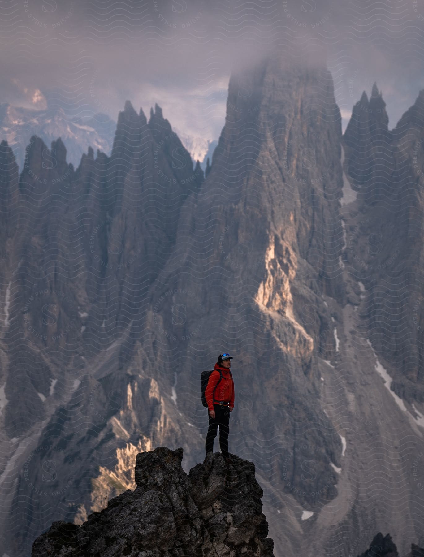 A person wearing dark clothes and a red coat, standing on top of a rocky peak during sunset.