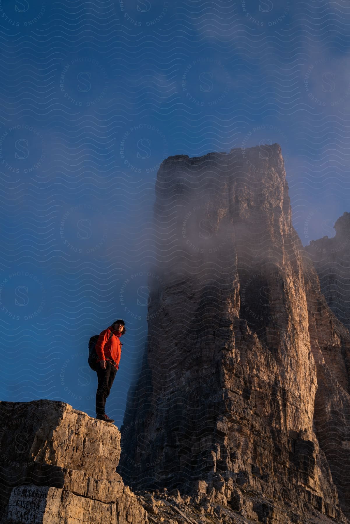 Hiker wearing a backpack standing on a mountain cliff near a tall rock formation