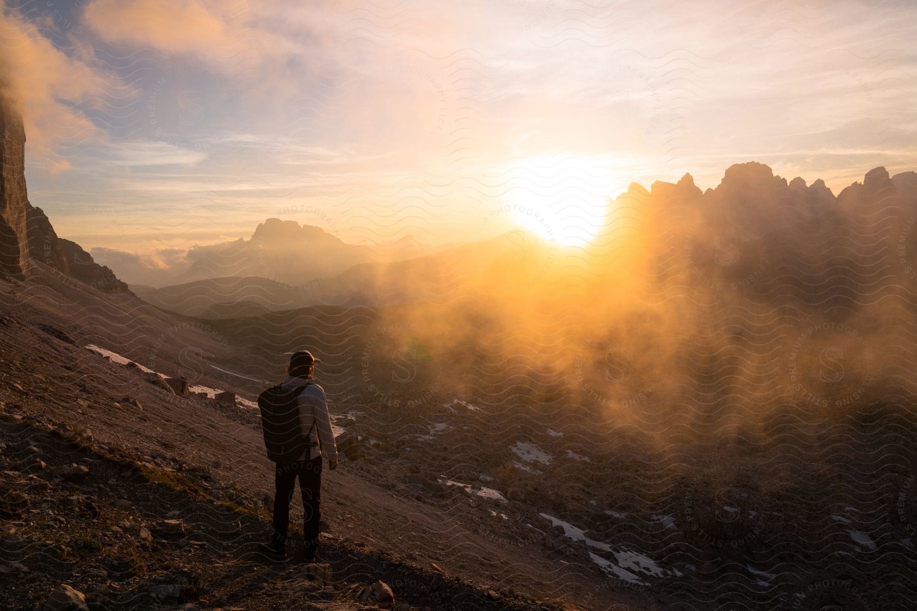 A hiker stares at the sun as it rises over a mountain range.