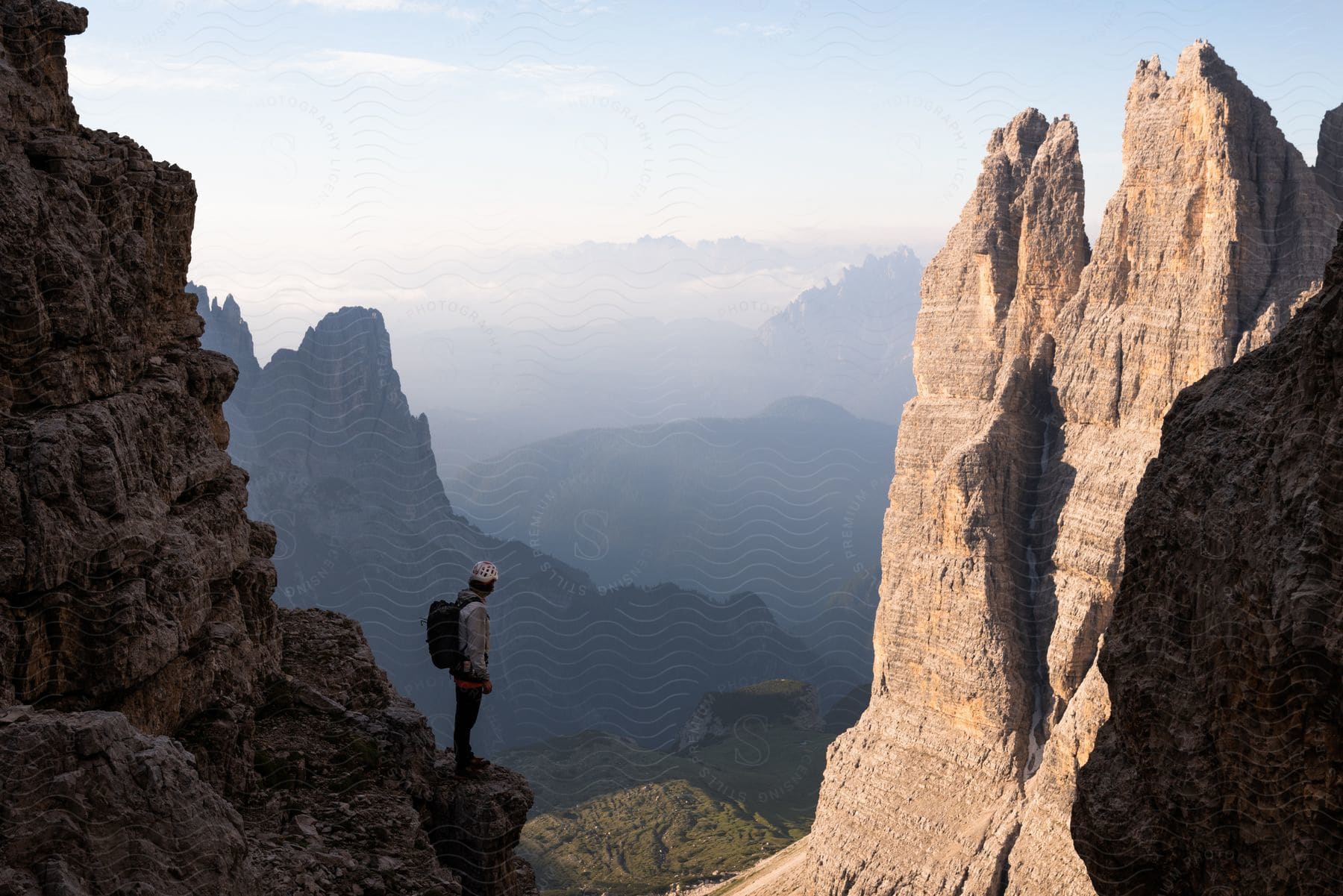 A hiker stands on a narrow rock shelf in a steep mountain range.