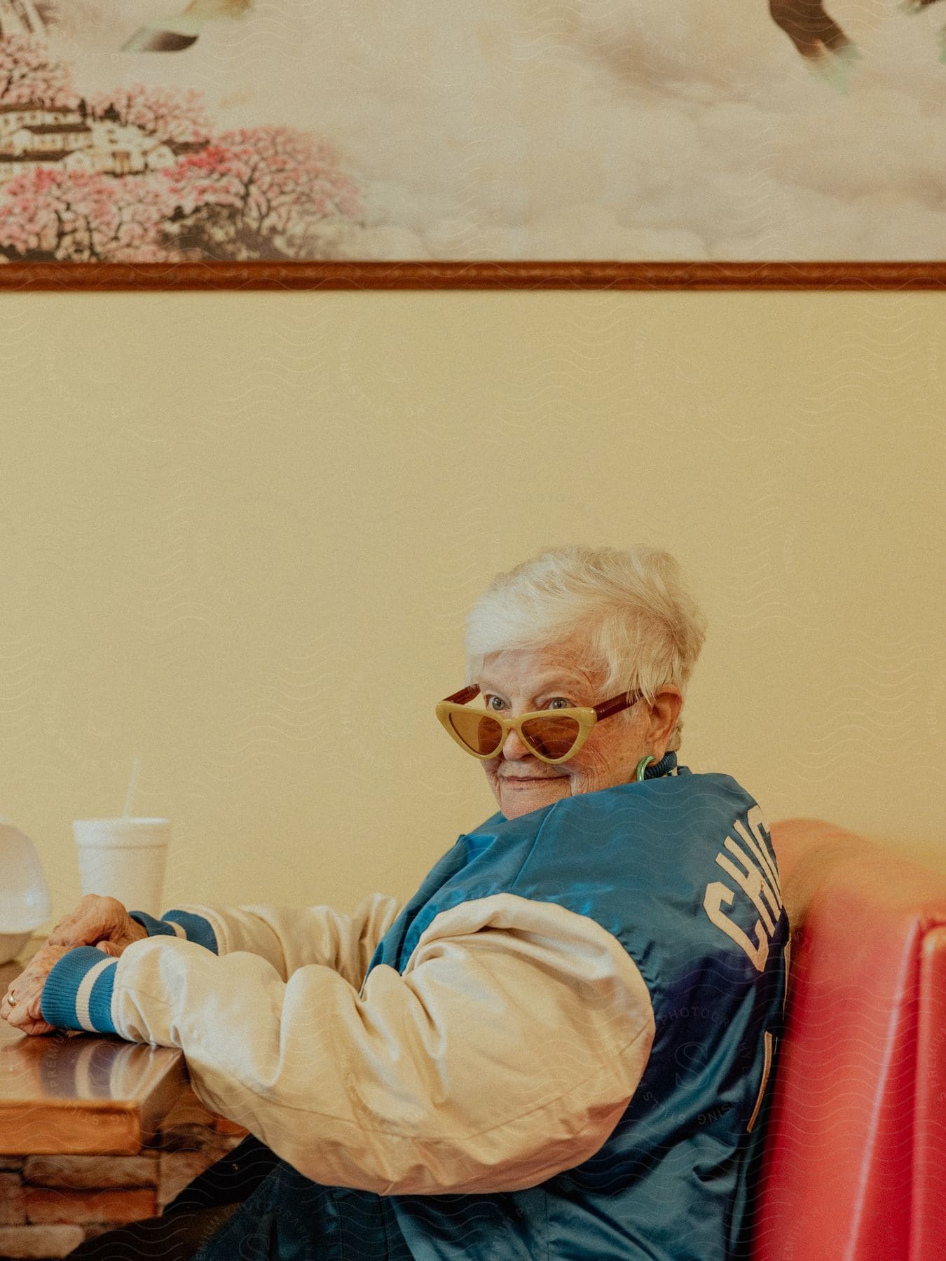 An elderly woman sits behind a desk at a dinner table with a coffee cup on the table.