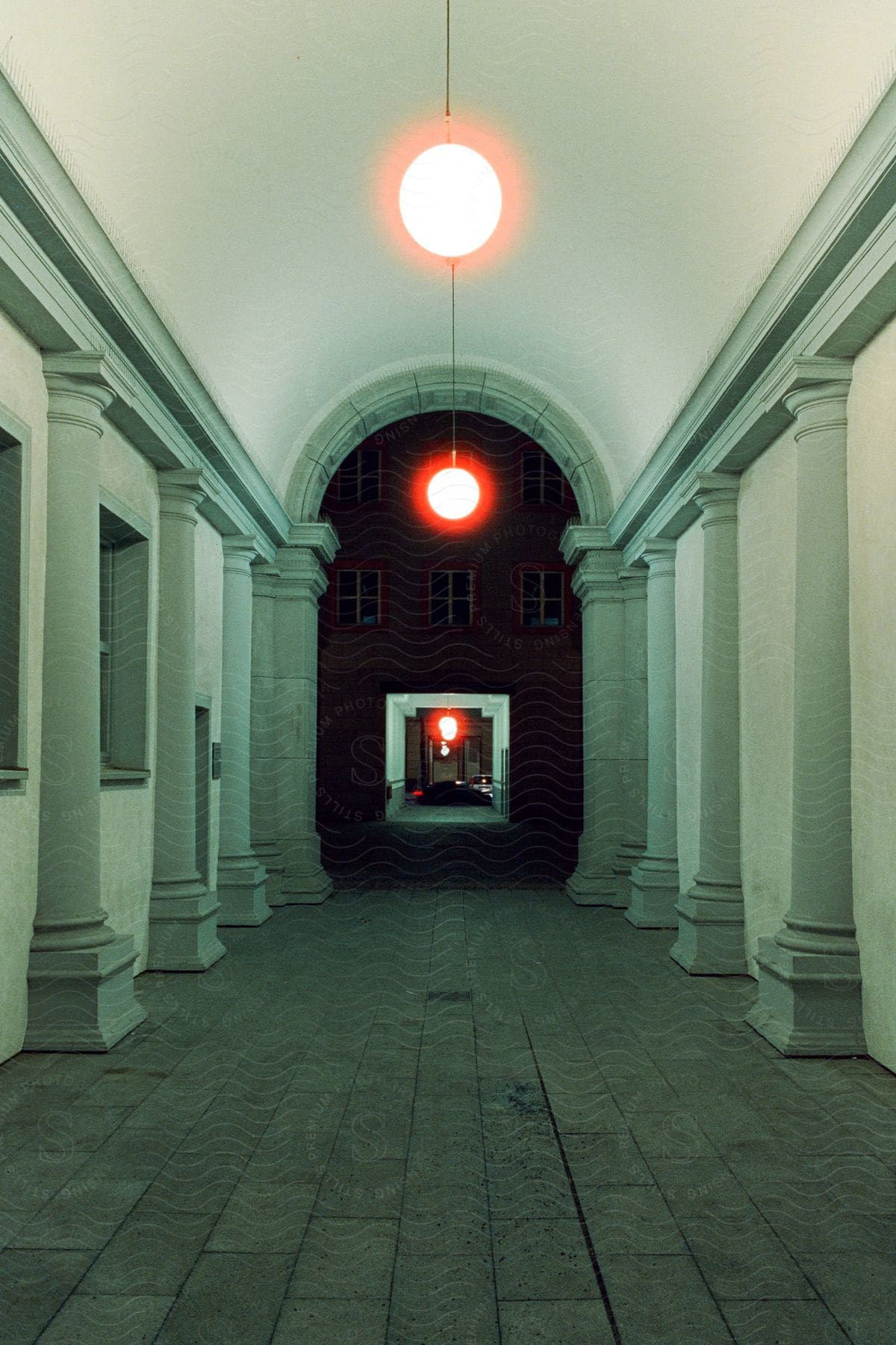 Symmetrical corridor with archways and hanging red lights.